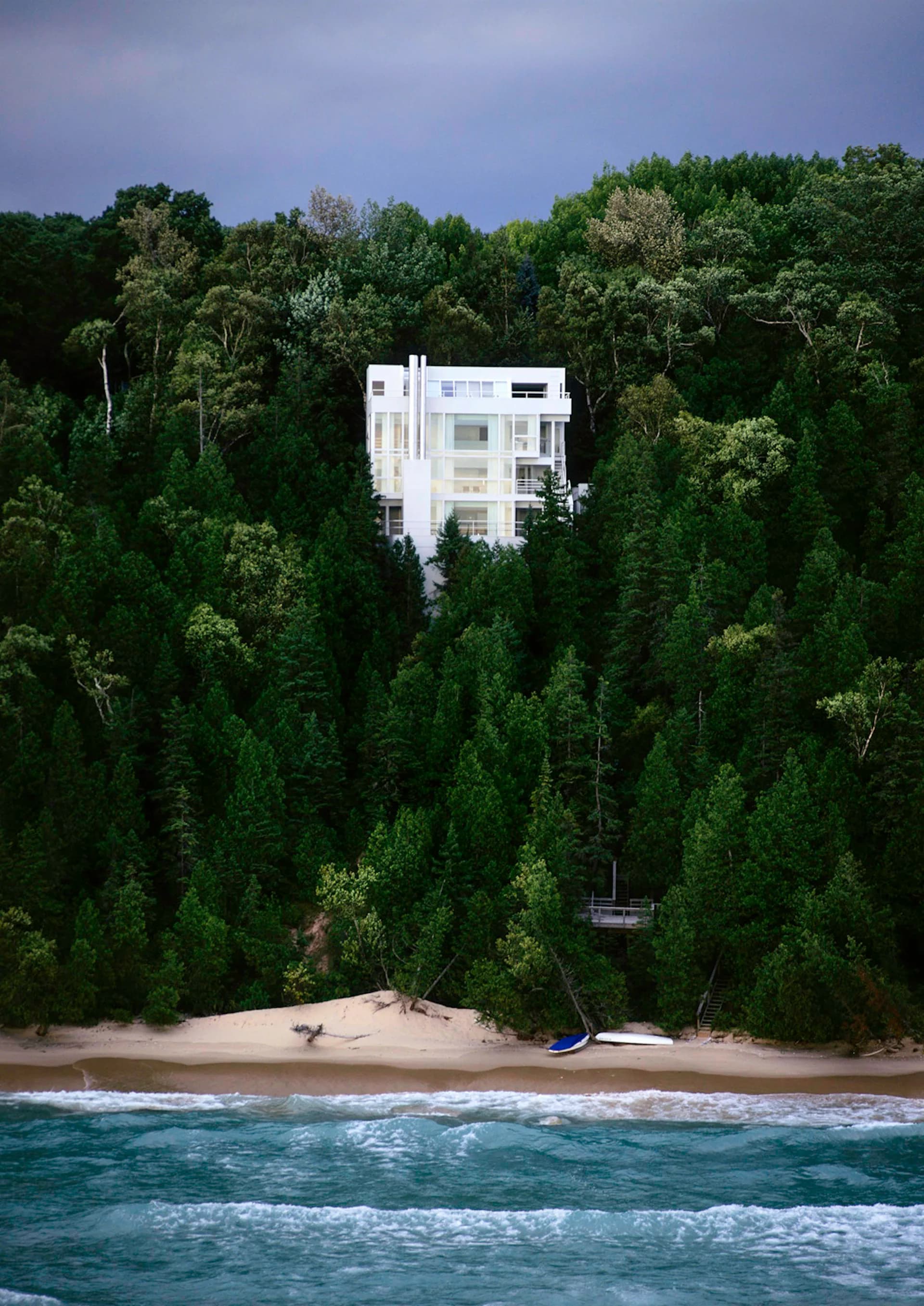 White modernist residence elevated above a dense forest canopy overlooking a sandy beach and ocean, by Meier Architects.