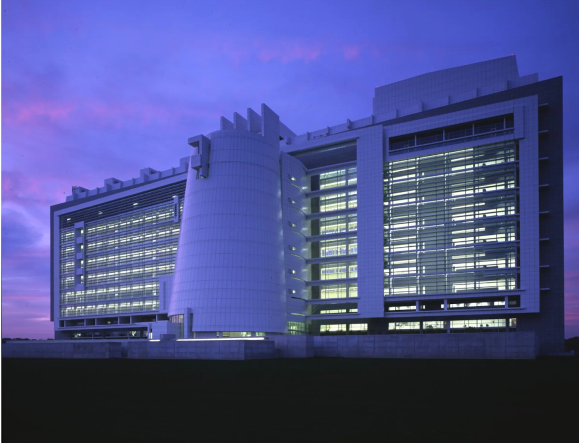 Illuminated modern institutional building with geometric facades and grid-patterned windows against purple twilight sky, designed by Meier Architects.