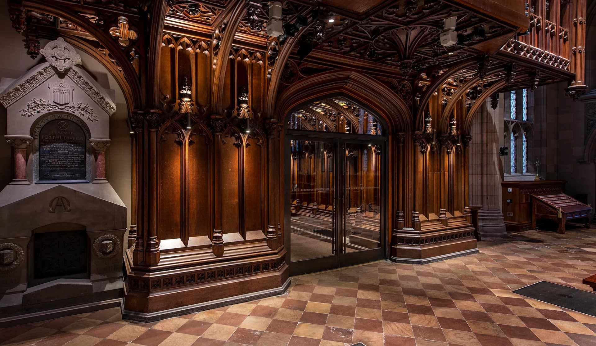 Ornate wooden interior with arched doorways, classical columns, and decorative ceiling, illuminated by warm architectural lighting by Melanie Freundlich Lighting Design.