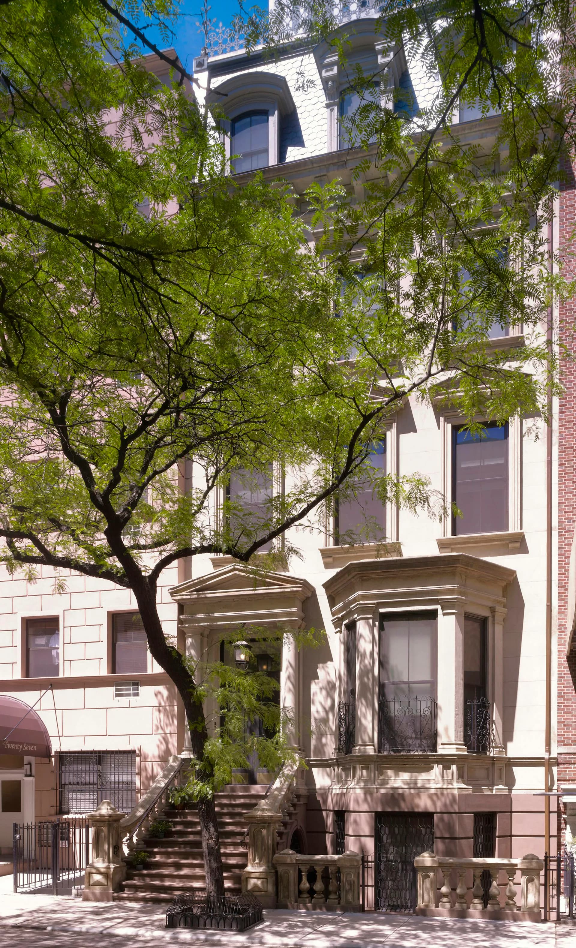 Restored historic brownstone facade with arched entrance, limestone and brick materials, and mature tree in front by MERGAL ARCHITECTURE & DESIGN.