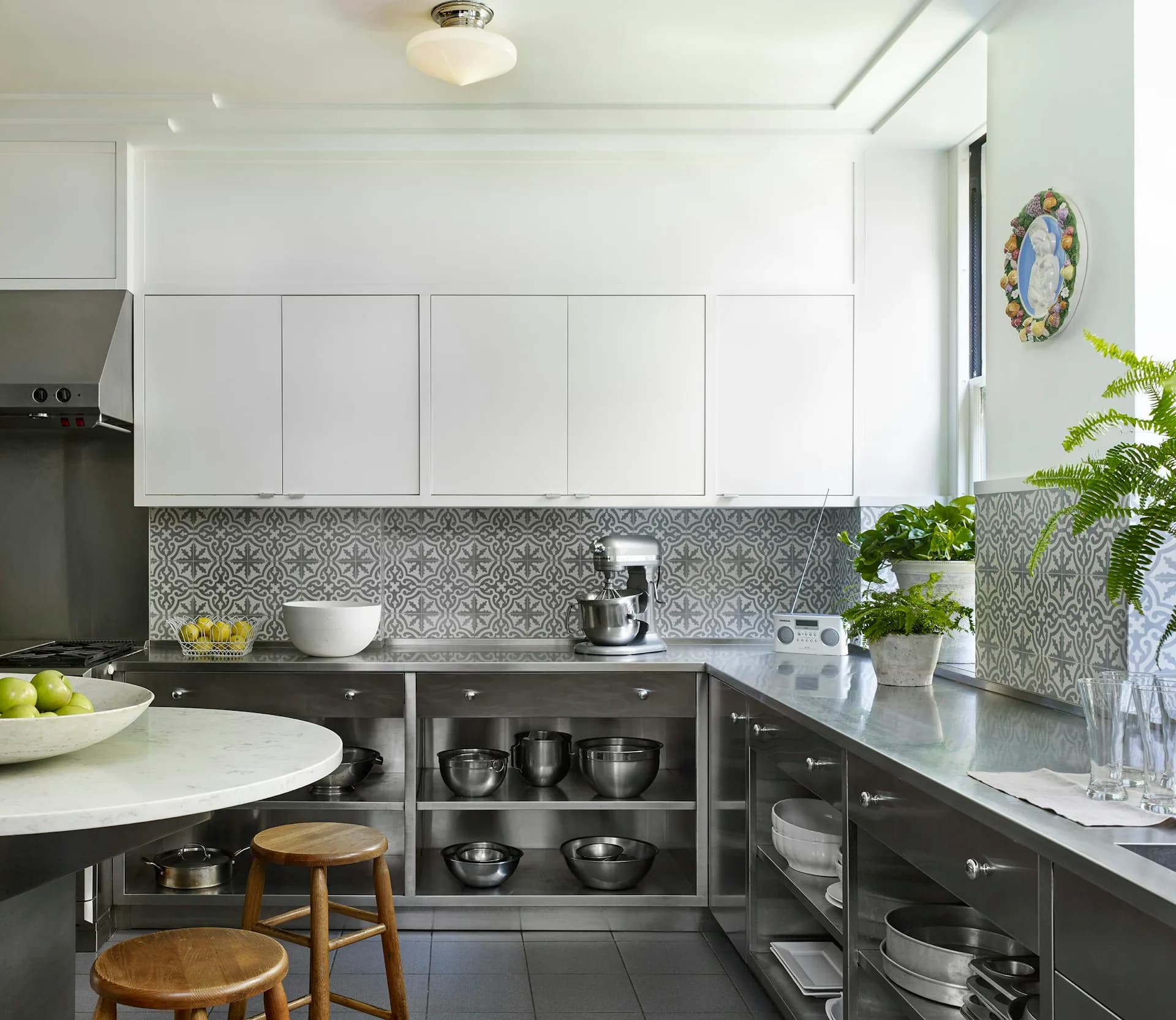 Modern kitchen featuring white upper cabinets, dark lower cabinetry, patterned tile backsplash, stainless steel appliances, and gray countertops by MERGAL ARCHITECTURE & DESIGN.