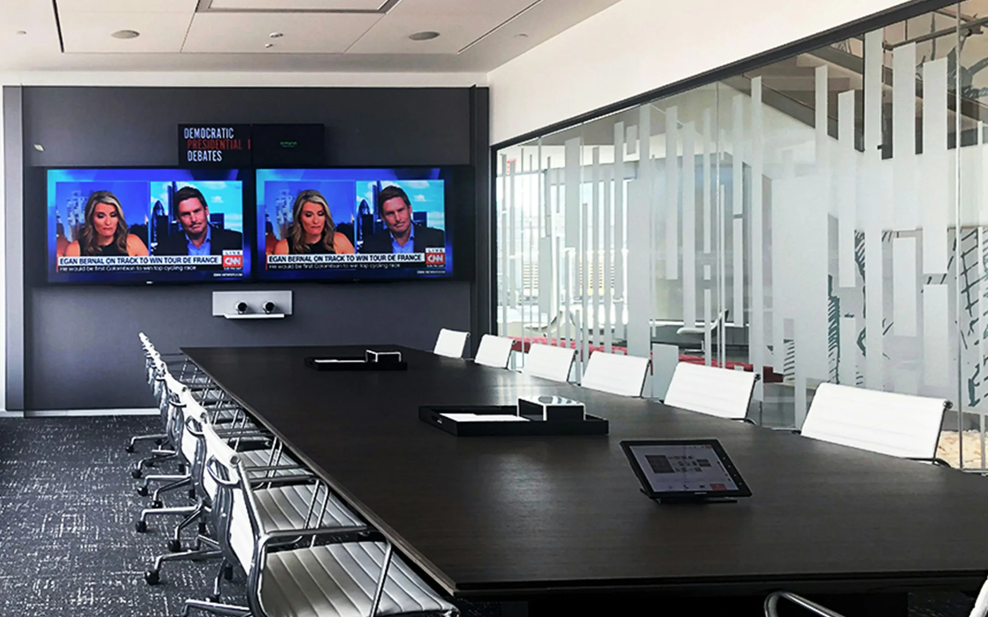 Modern conference room with black table, white chairs, dual mounted displays, glass partitions, and architectural blueprint details on walls by Meridian Design Associates, Architects, P.C.