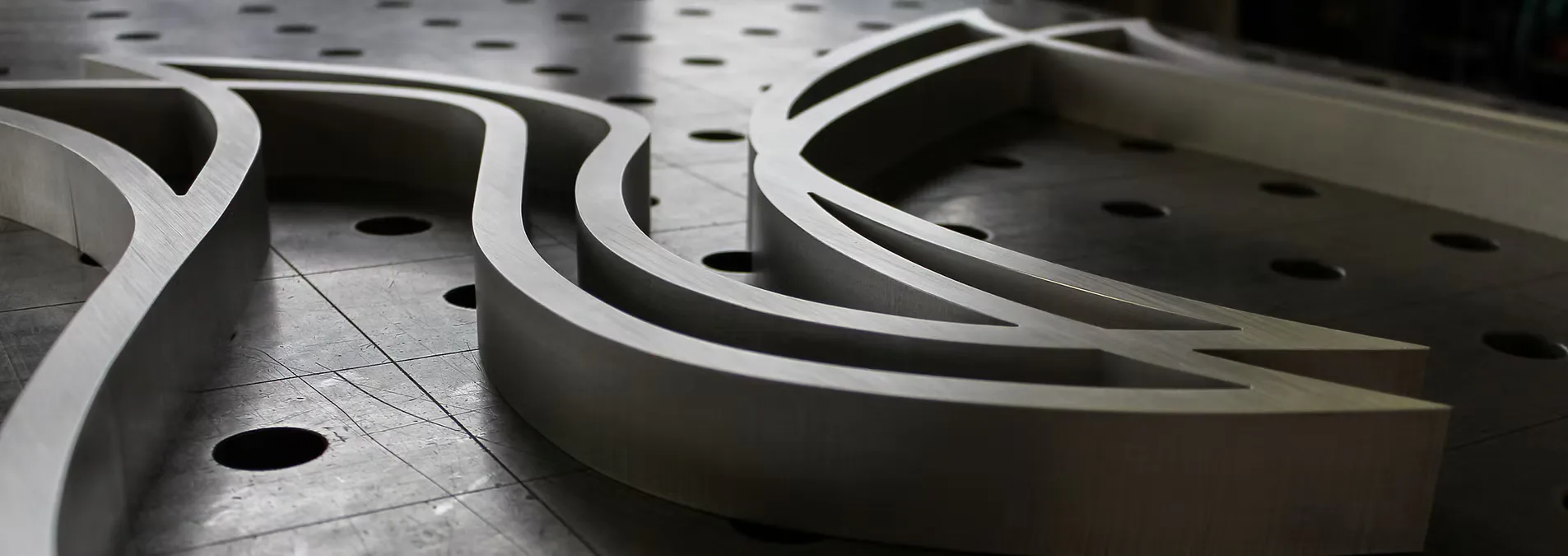 Close-up of curved white metal architectural elements with perforated surfaces and dramatic shadows, showcasing precision metalwork by Metalform Studio.