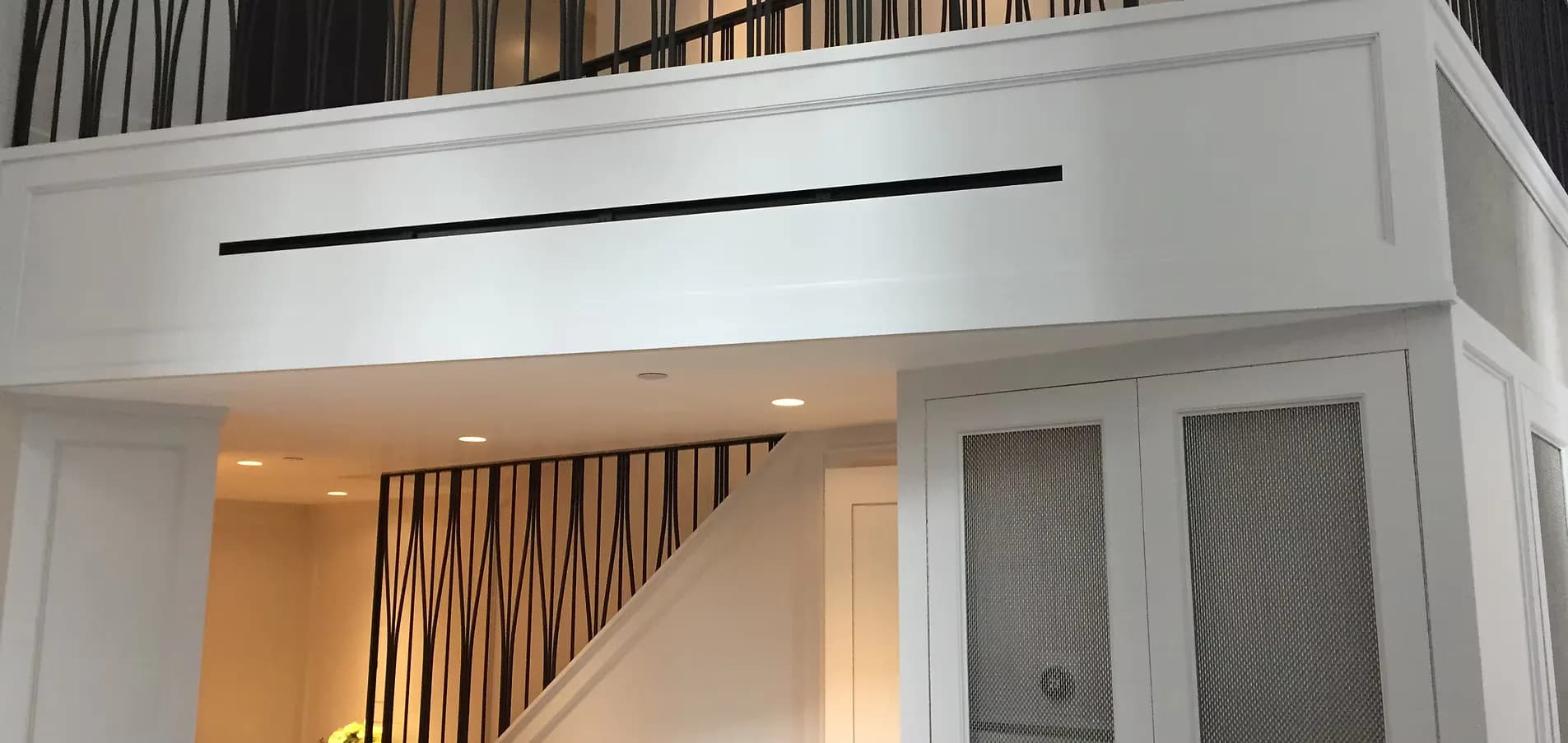 Modern white interior staircase with geometric wood slat railing detail and recessed lighting by Metalform Studio.