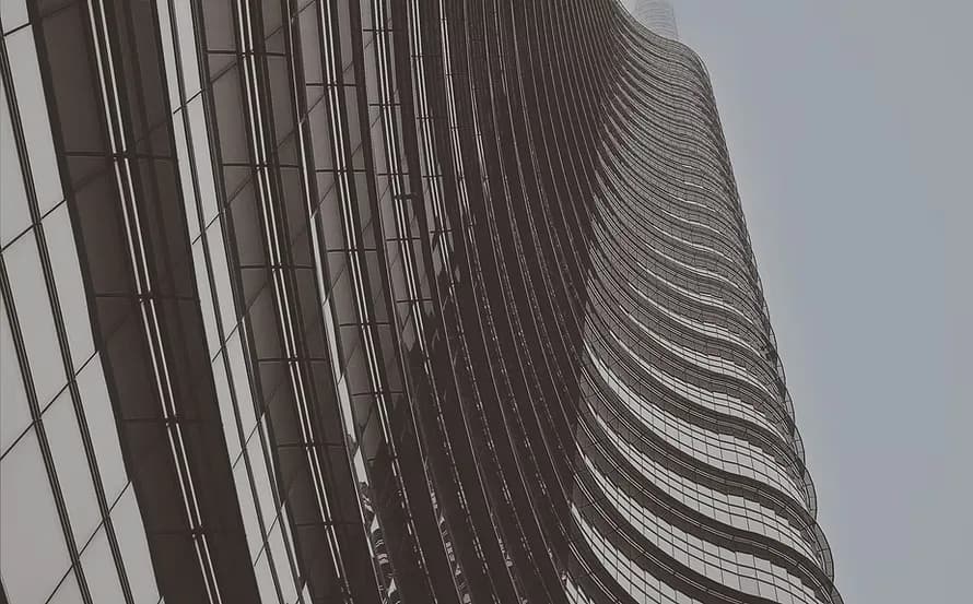 Curved modernist facade with rhythmic horizontal ribbing and striped window pattern photographed from below against overcast sky by Metalform Studio.