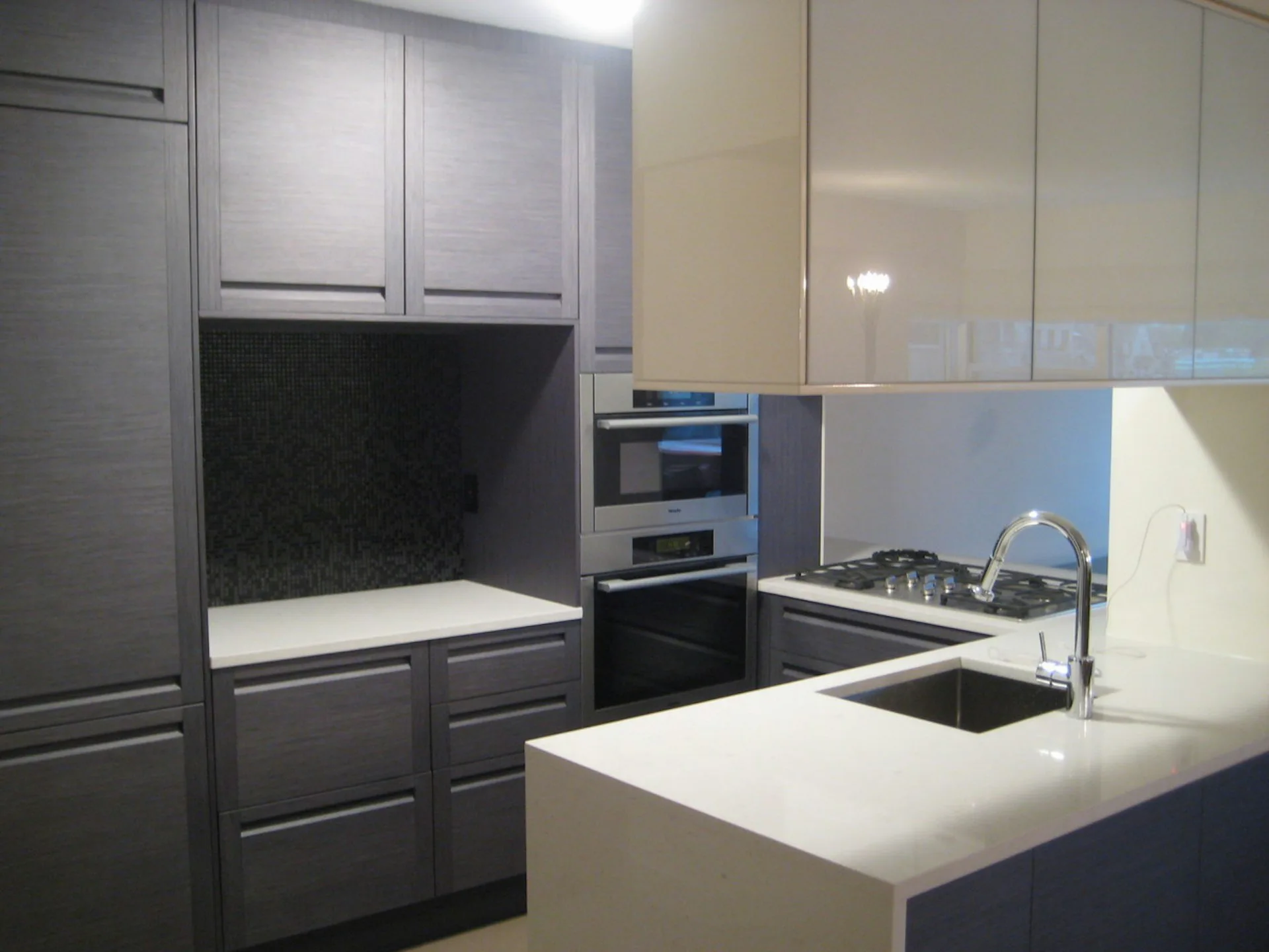 Modern kitchen with dark cabinetry, white countertop island, stainless steel appliances, and glossy upper cabinets, designed by Metropolitan United Studio, PLLC.