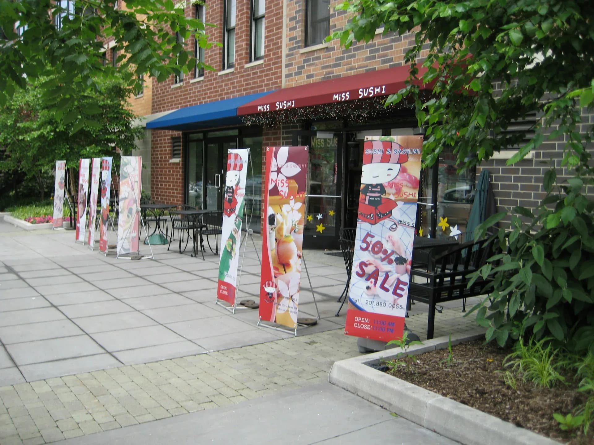 Storefront window display featuring colorful sale banners and floral graphics on a brick facade with green ivy, designed by Metropolitan United Studio, PLLC.