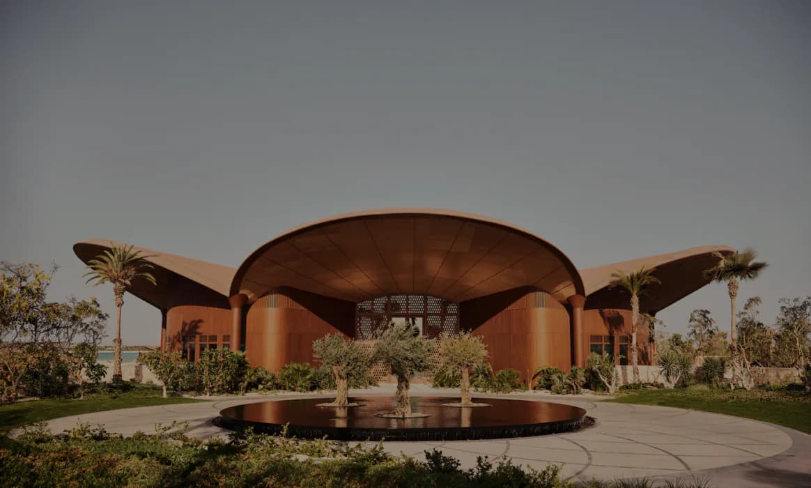 Large-scale copper pavilion with dramatic curved surfaces set in a landscaped plaza with palm trees and water features, designed by Meyer Davis.