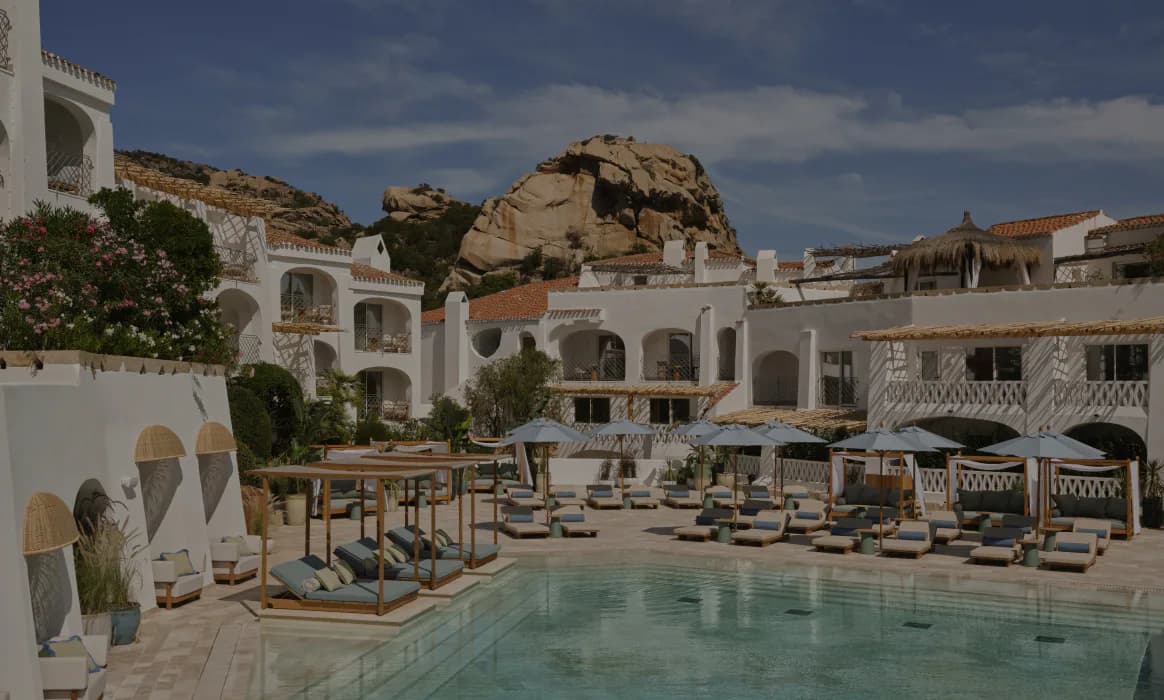 Luxurious resort pool courtyard with white Mediterranean architecture, natural stone boulders, lounge seating, and blue water by Meyer Davis.