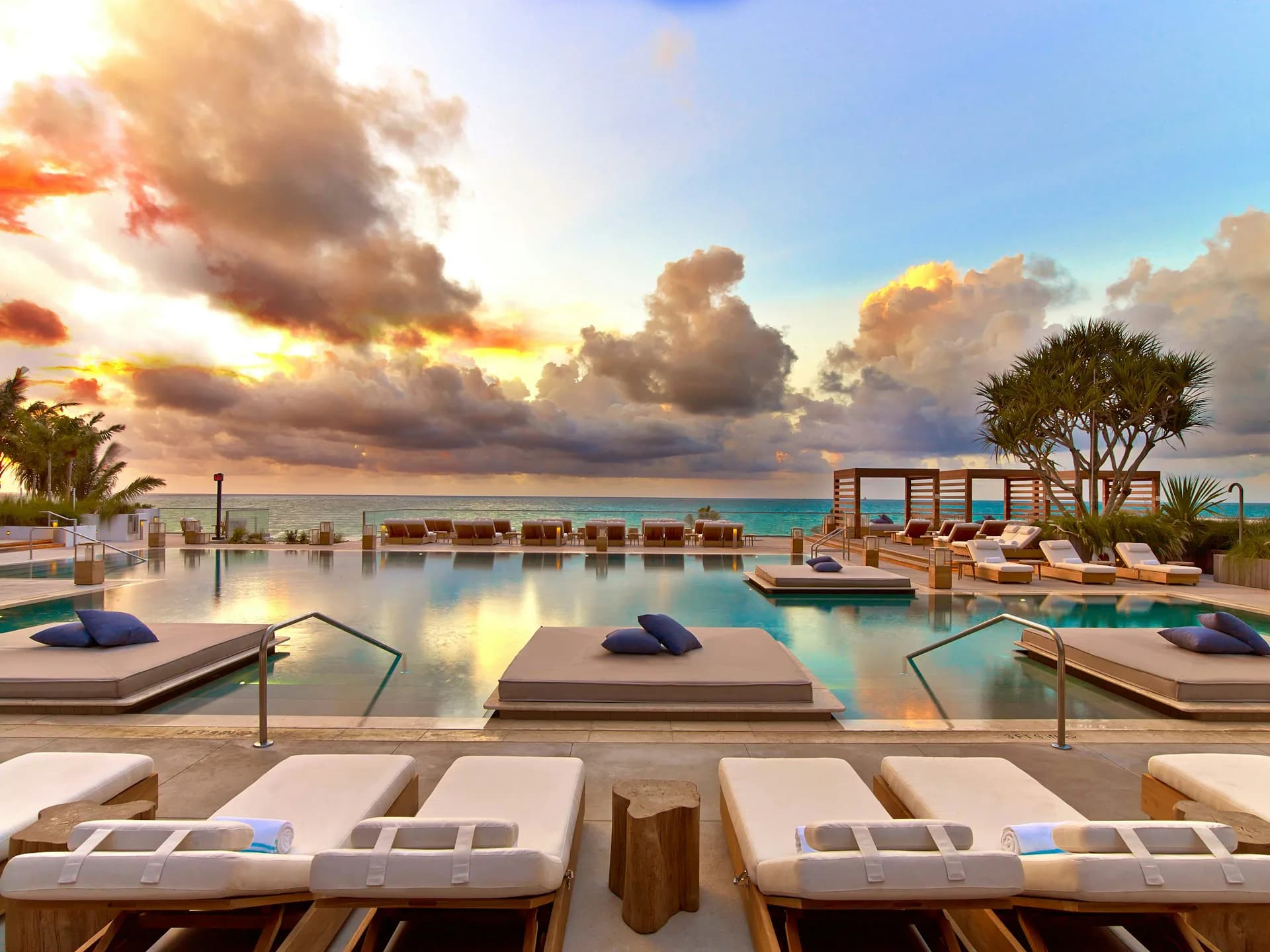 Waterfront resort pool deck at sunset with loungers, infinity pool, and tropical landscaping by Meyer Davis Studio Inc.