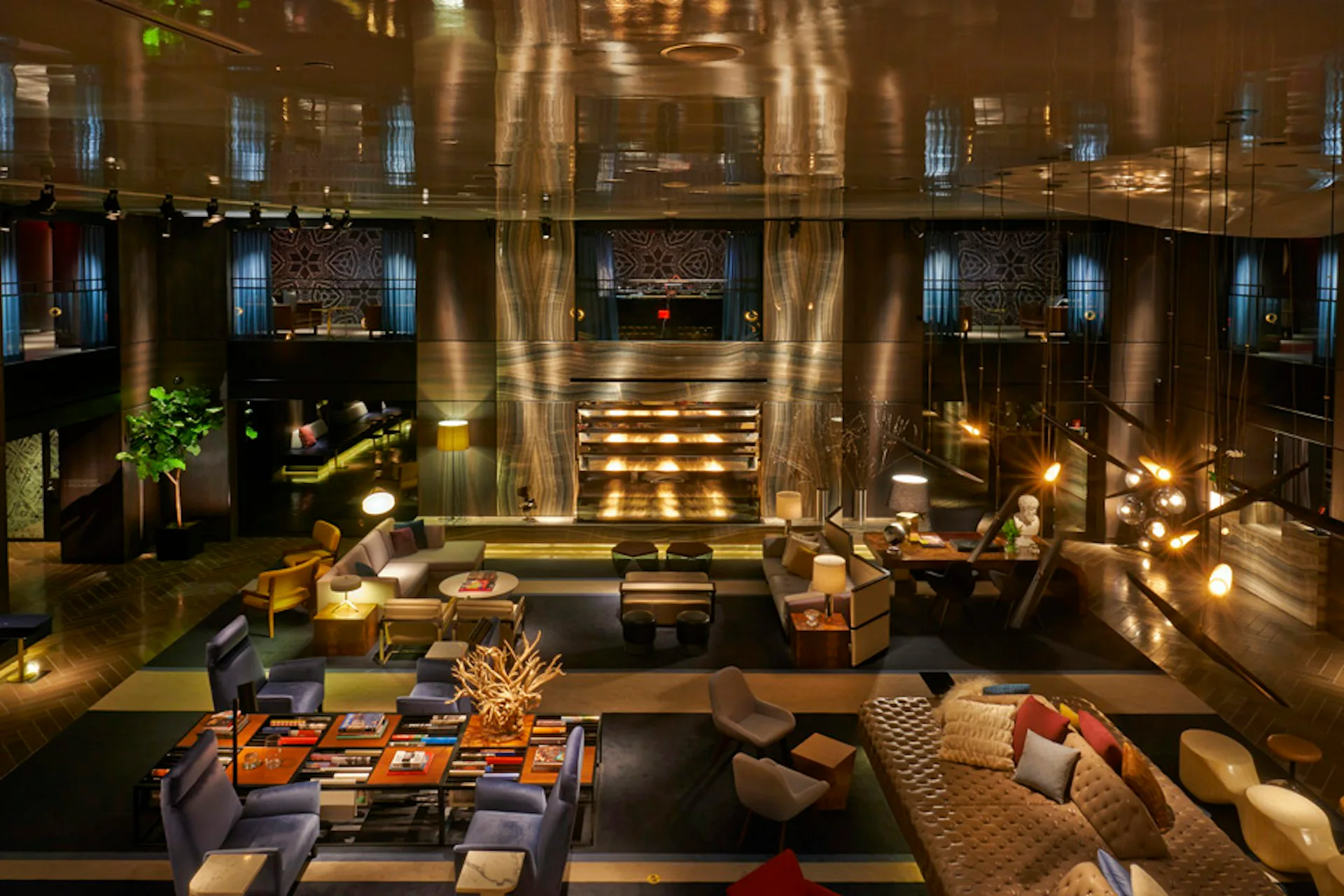 Luxurious hotel lobby with warm golden lighting, multi-level atrium, contemporary furnishings, and architectural column details by Meyer Davis Studio Inc.