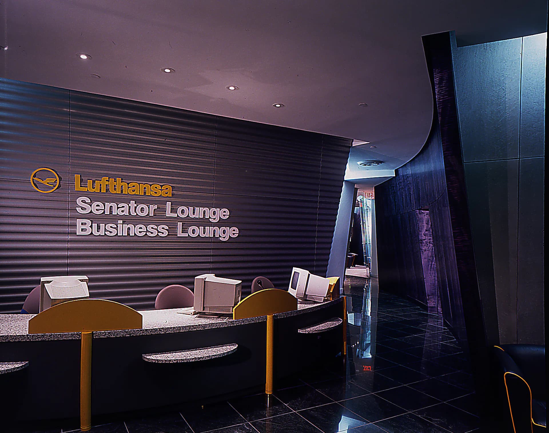 Lufthansa Senator Lounge and Business Lounge reception area featuring a dark horizontal-slat accent wall, wood furnishings, modern lighting, and sleek black flooring by Michael McDonough Architect.