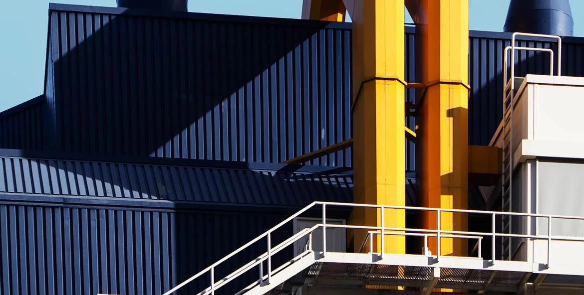 Industrial architectural exterior featuring bold yellow structural columns and dark metal corrugated siding with white metal railings and platforms by Milgo/Bufkin.