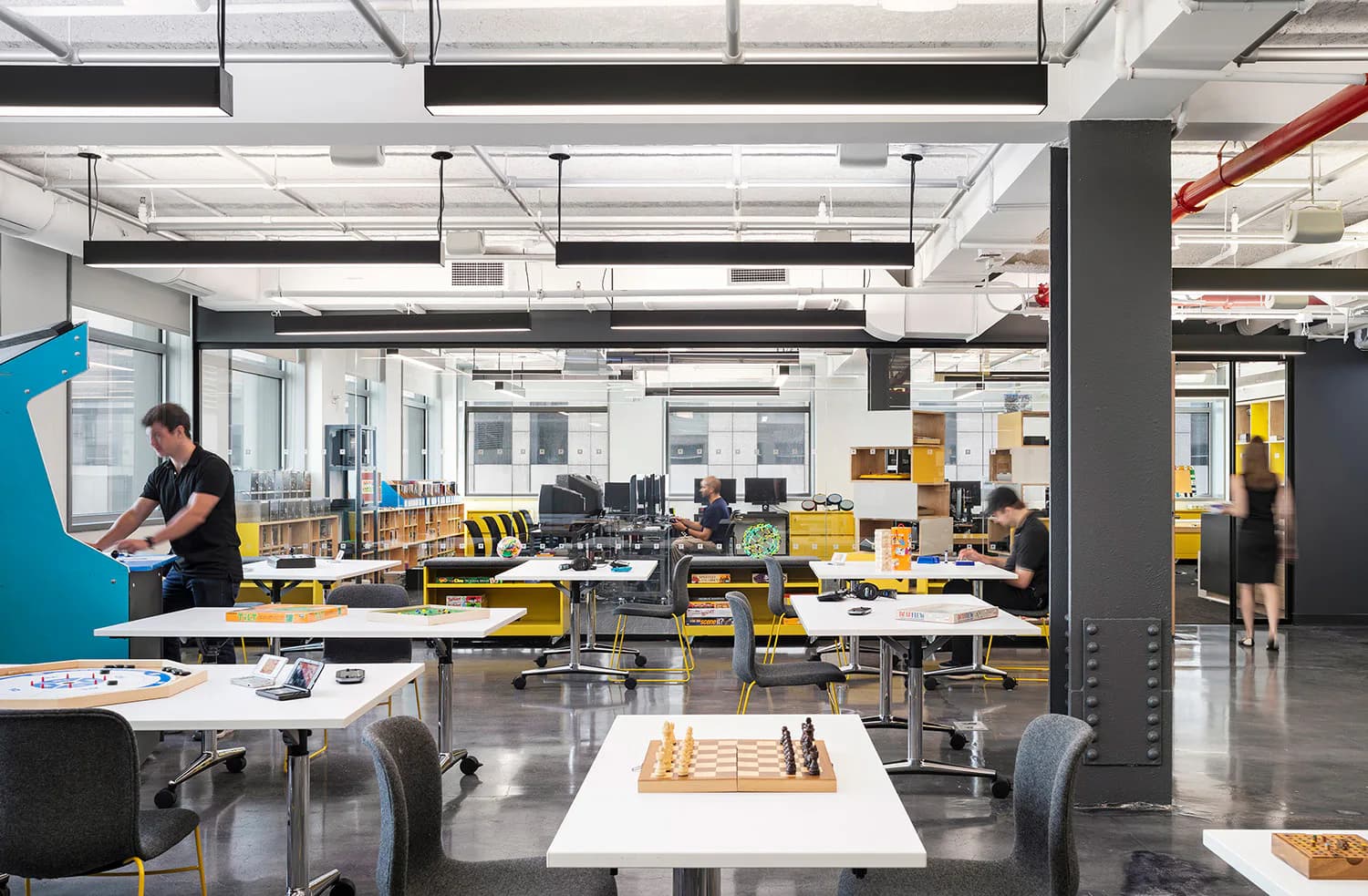 Modern office workspace with yellow desks, concrete columns, and glass partitions creating an open collaborative environment by Mitchell Giurgola.