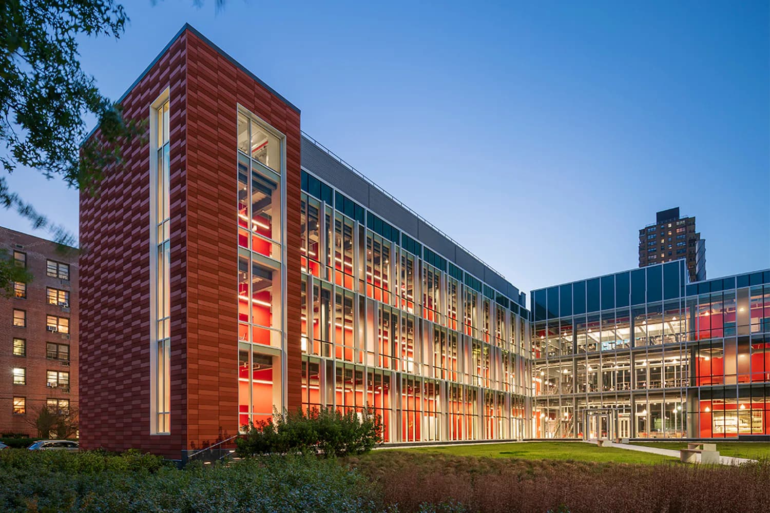 Modern institutional building with red brick tower and illuminated glass curtain wall facade photographed at dusk, designed by Mitchell Giurgola.