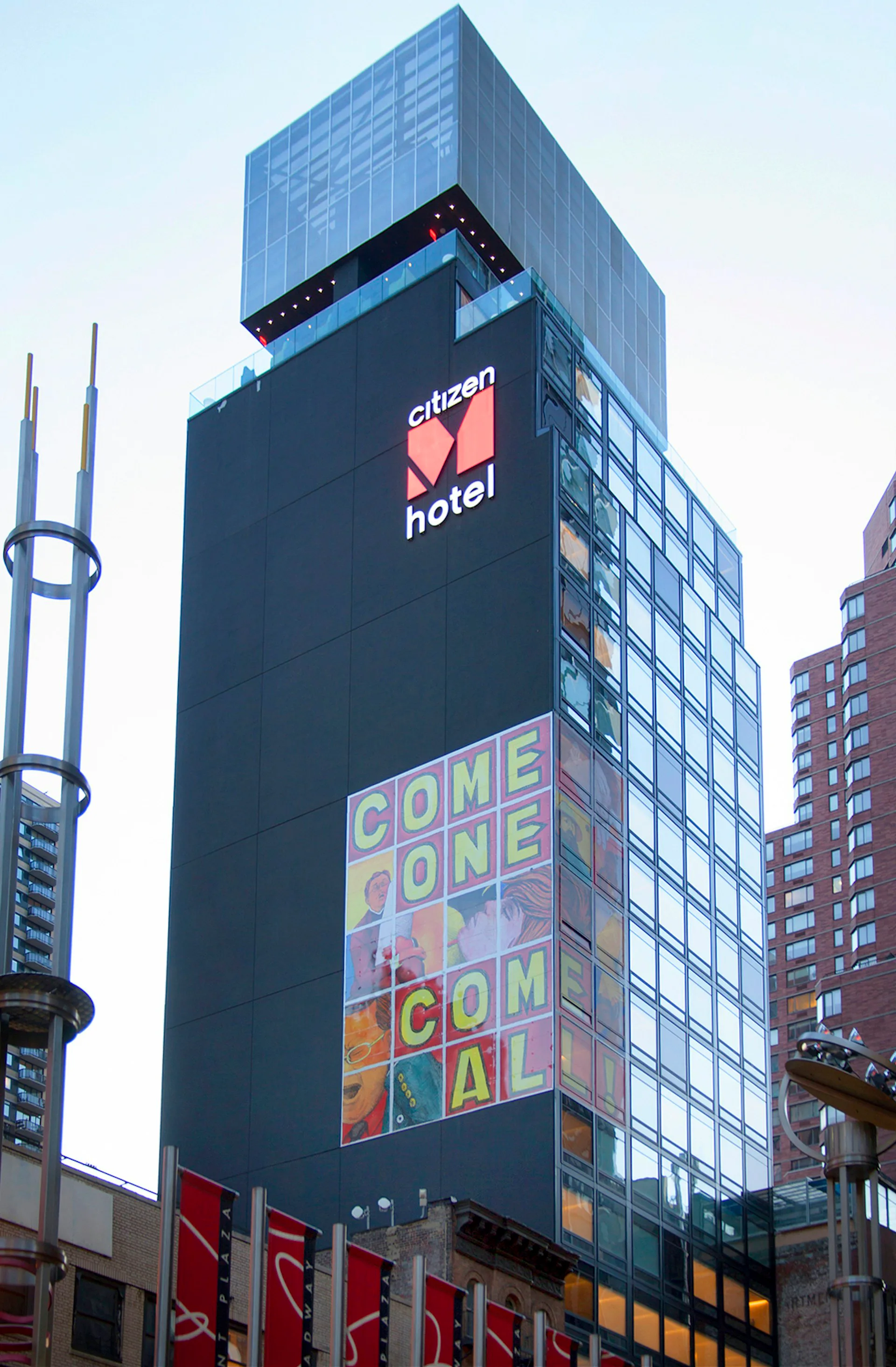 Tall urban hotel tower with dark facade featuring colorful digital signage displaying 'Citizen Hotel' and promotional messaging, surrounded by neighboring buildings in an urban streetscape.