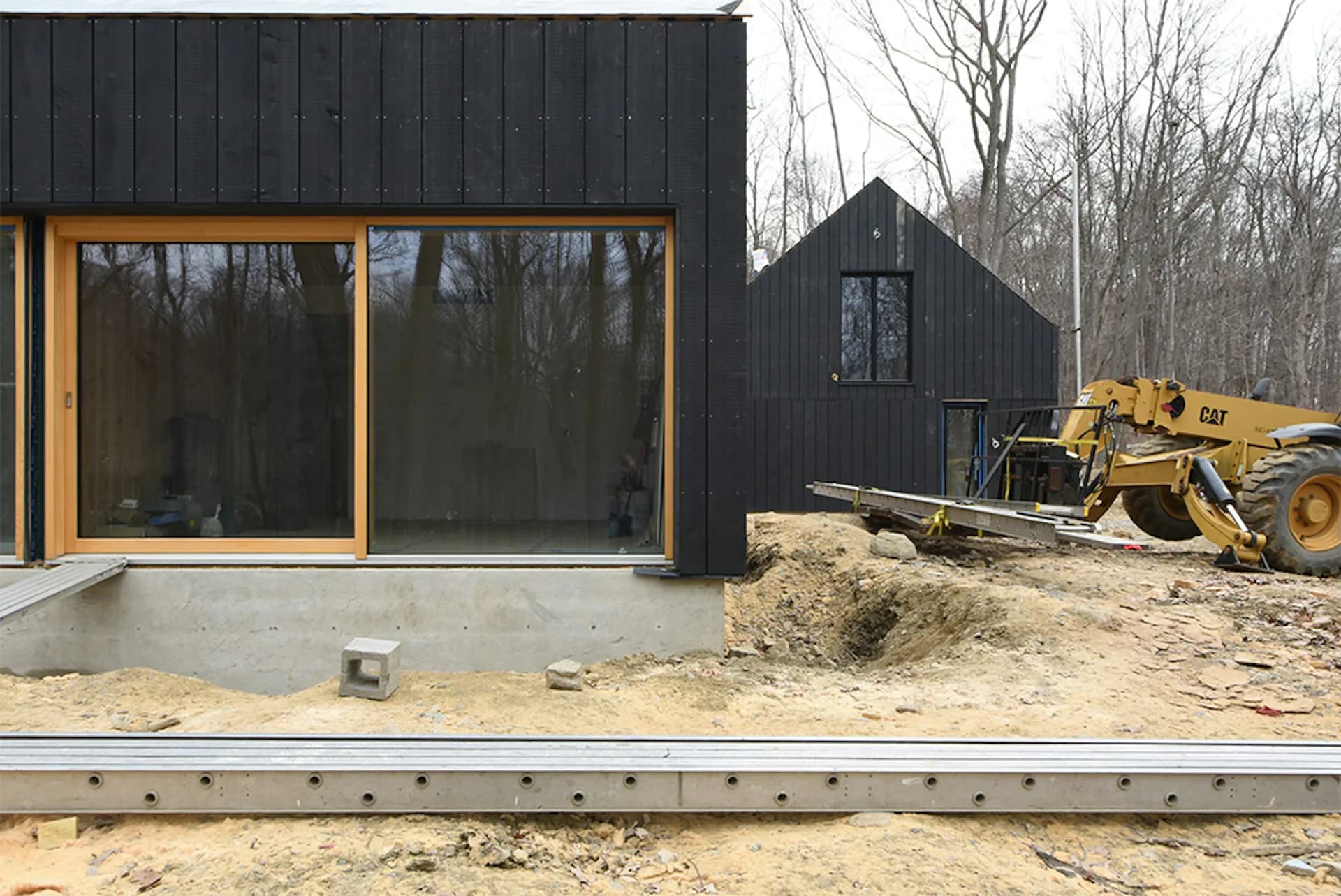 Modern black residential building with golden-framed glazing under construction, surrounded by earth and machinery, by MOREMAS.