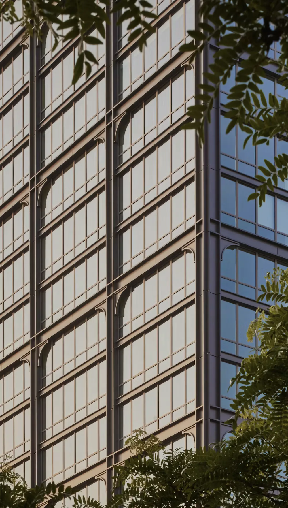 Facade of a modernist building featuring repetitive steel-frame windows with geometric grid patterns and decorative metal mullions, framed by vegetation, by Morris Adjmi Architects.