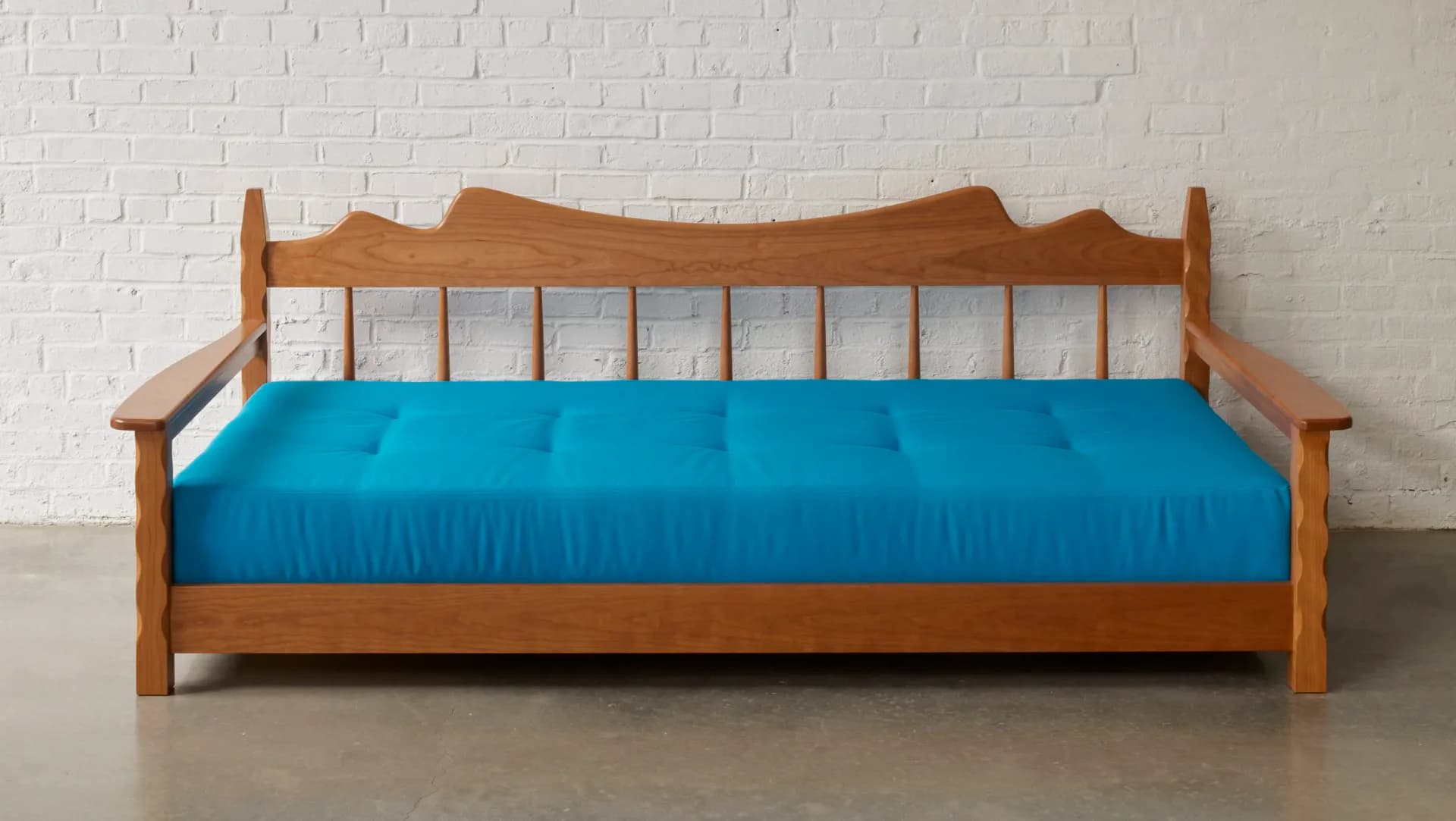 Wooden daybed with turquoise upholstered mattress and white spindle backrest against white brick wall by Moving Mountains.