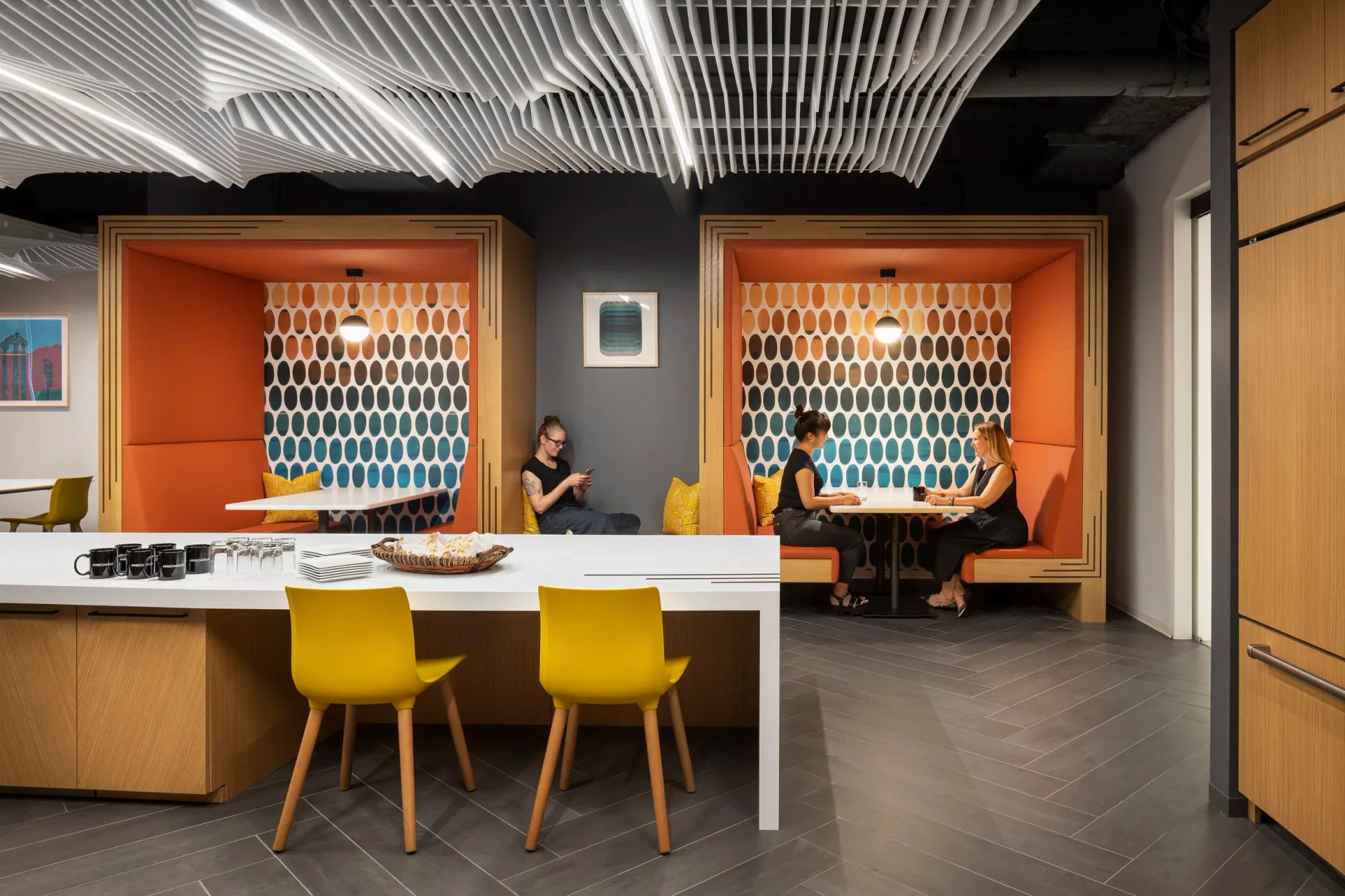 Modern office reception area with orange accent walls, white desk, yellow chairs, and geometric patterned backdrop lighting design by MRD Lighting.