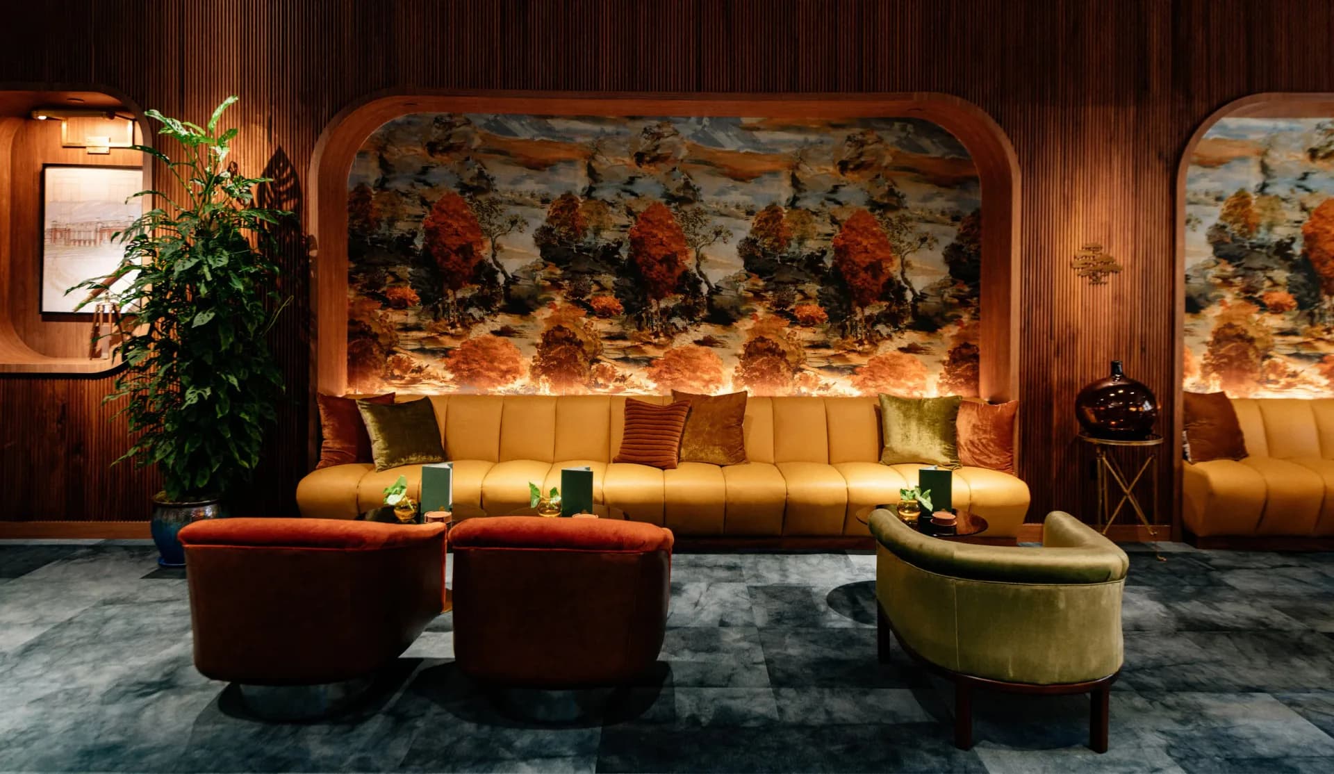 Warm-toned lounge interior with golden upholstered seating, leather ottomans, decorative murals, and ambient lighting design by MRD Lighting.