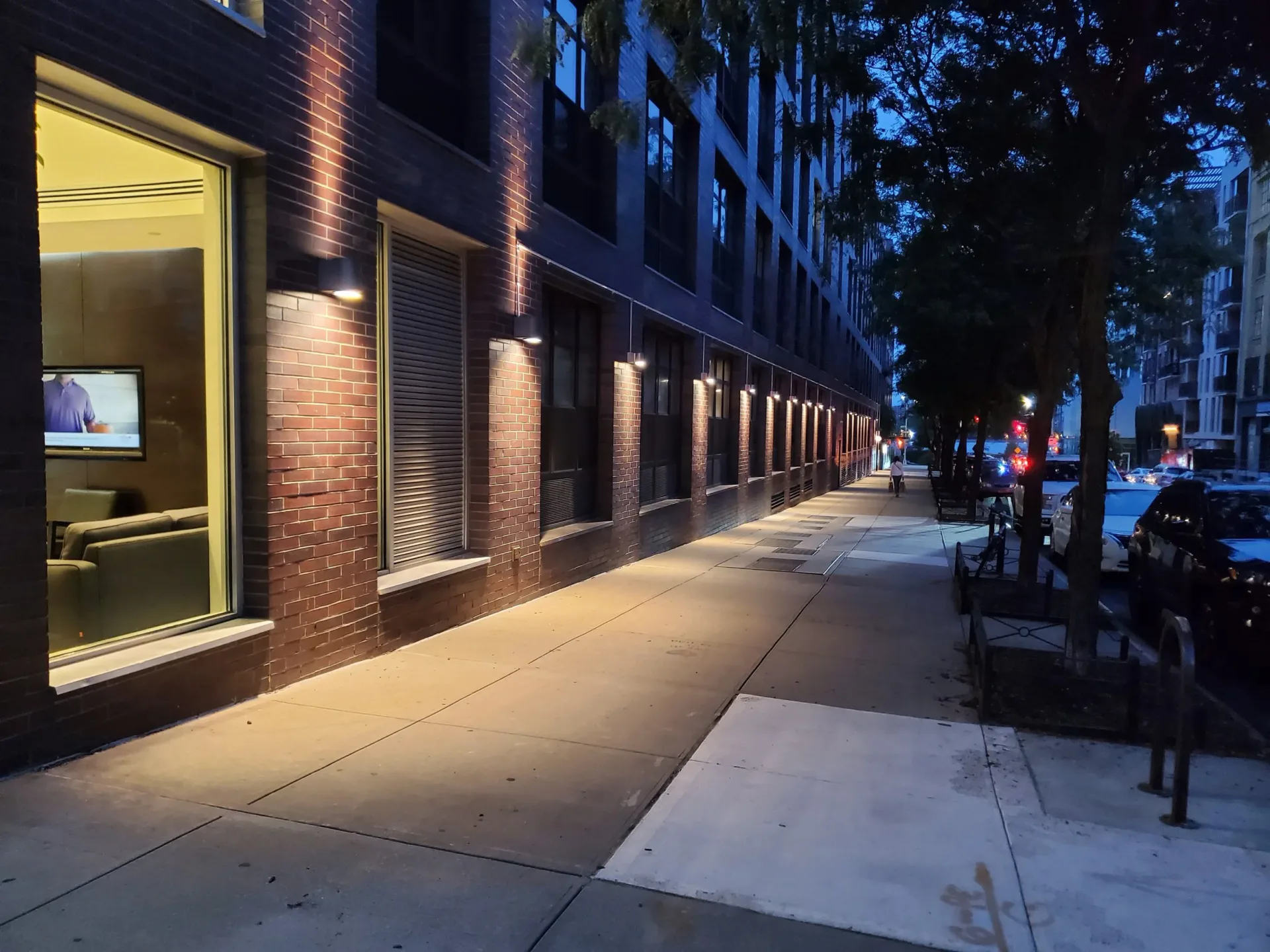 Nighttime street facade with warm-lit brick storefront and uplighting on architectural elements by MYLD Studio.