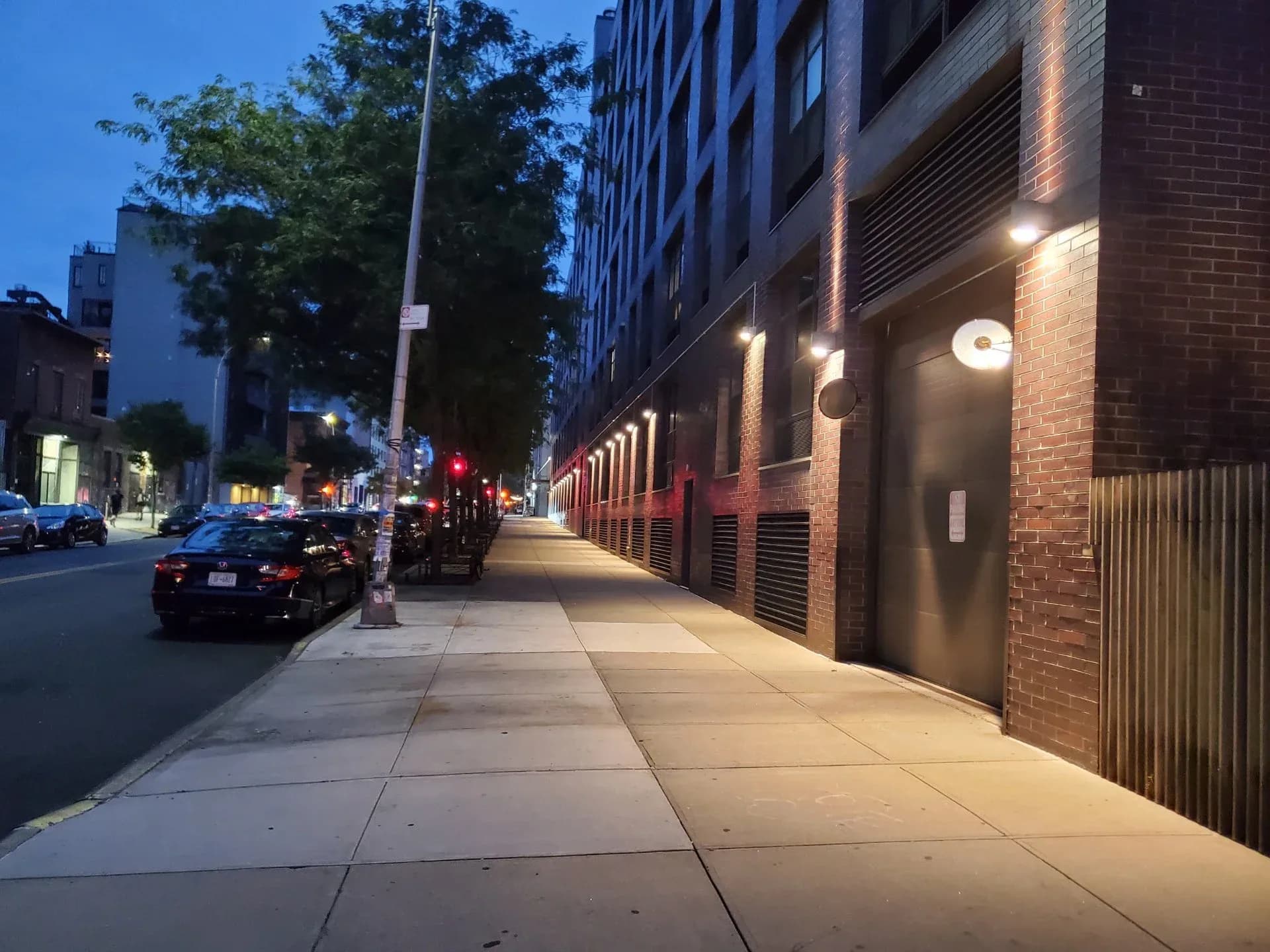 Urban streetscape at dusk featuring a brick building facade with illuminated wall sconces and dark storefronts, designed by MYLD Studio.