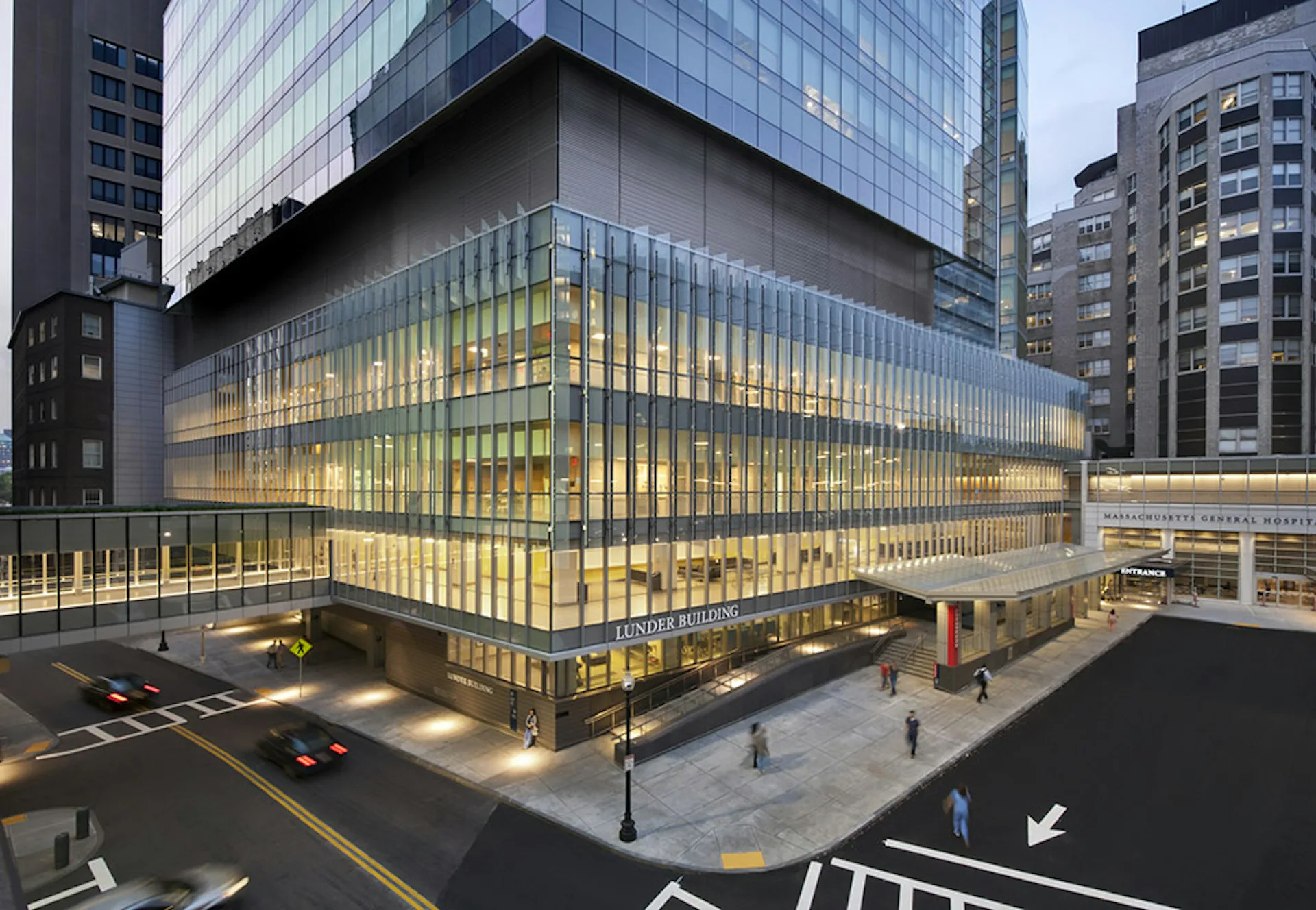Illuminated glass-and-steel commercial building facade with gridded window pattern and ground-level plaza by NBBJ.