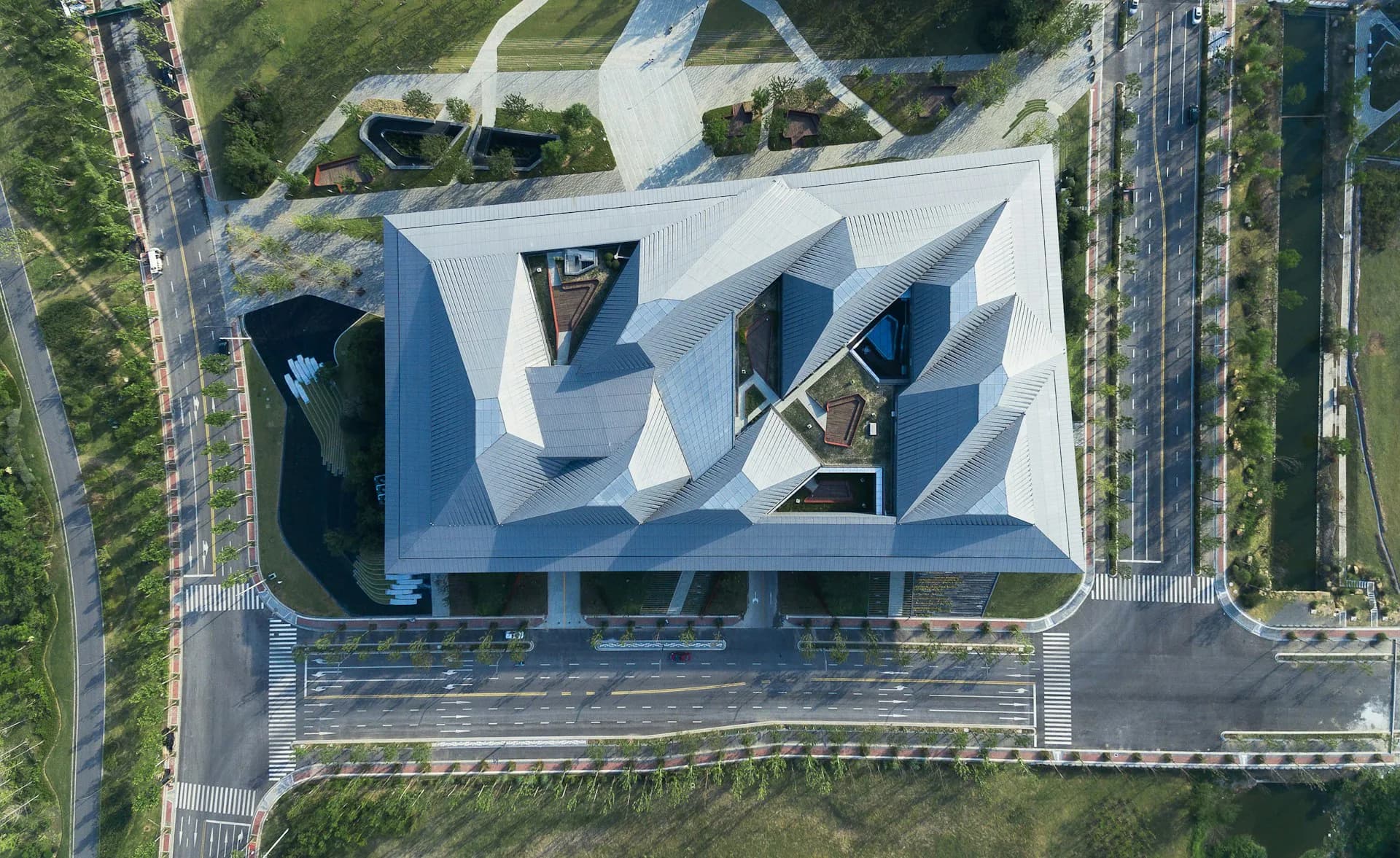 Aerial view of a white sculptural building with angular geometric forms and integrated green spaces, surrounded by residential towers by NBBJ.