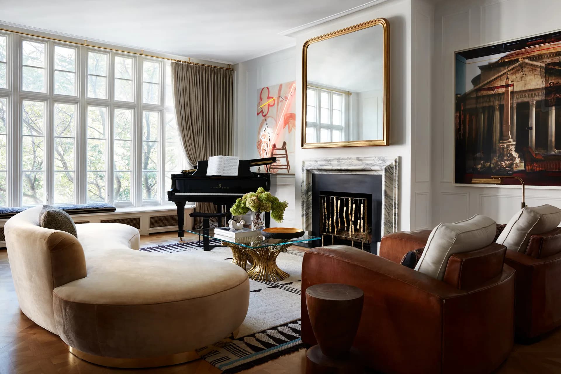 Elegant living room with cream curved seating, cognac leather chairs, grand piano, fireplace, and large windows overlooking gardens by Neal Beckstedt Studio.