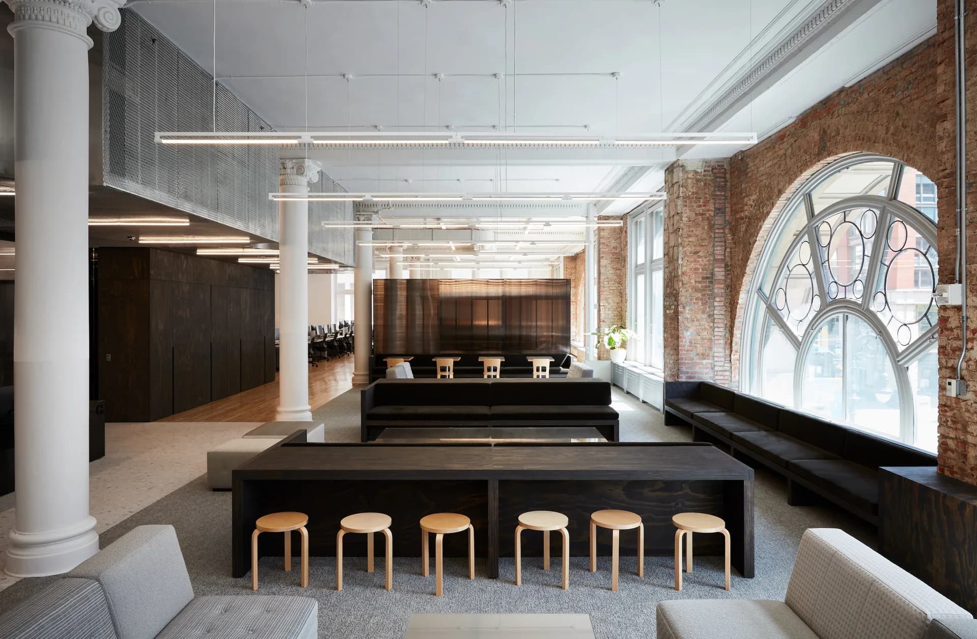 Modern restaurant interior with black counter, wooden stools, exposed brick wall, and large arched window by Neal Beckstedt Studio.