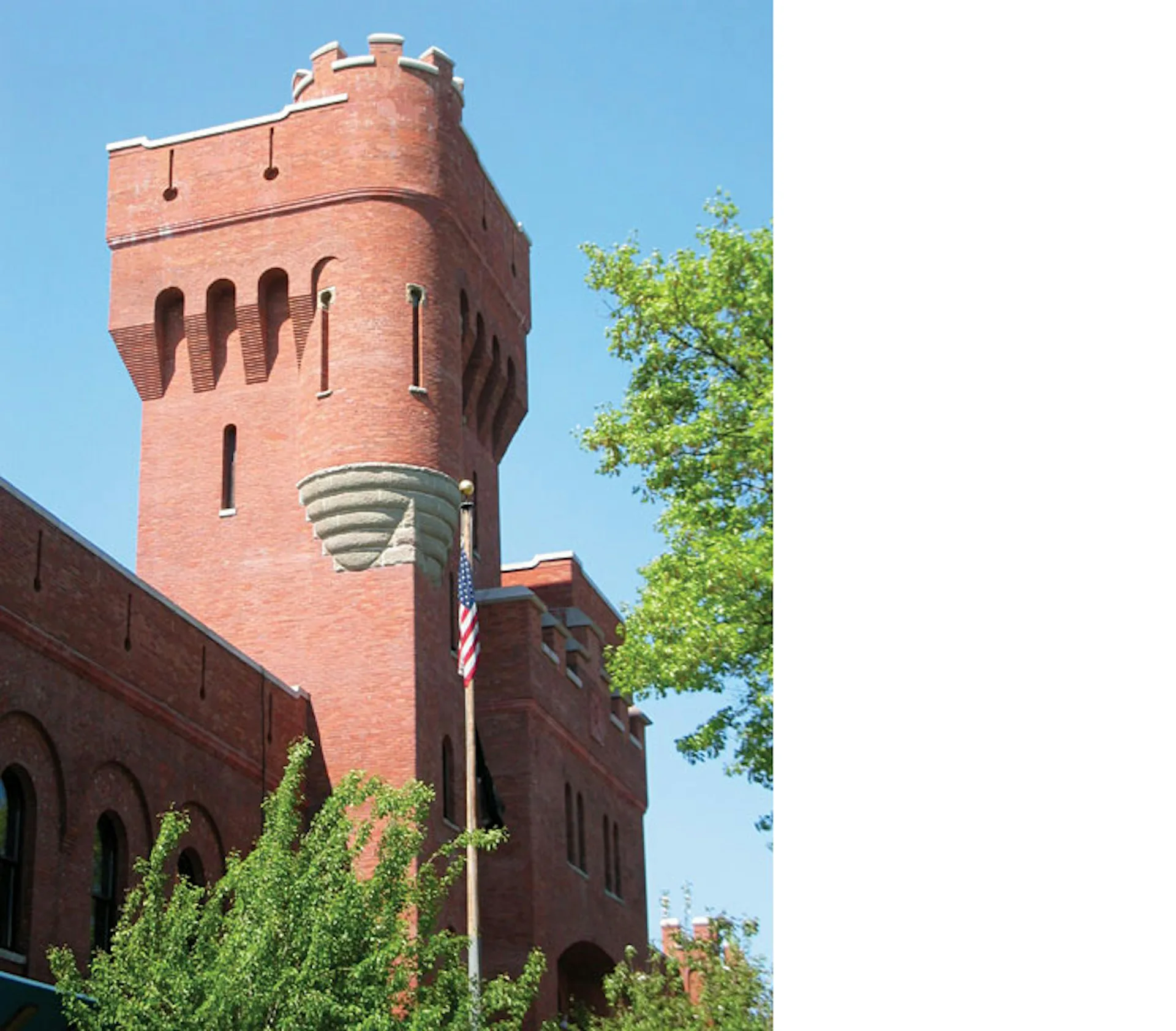 Red brick tower with crenellations and decorative banding, featuring arched openings and masonry detailing by Nelligan White Architects.