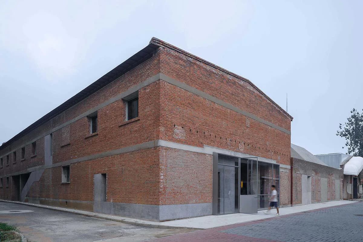 Red brick corner building with clean modernist lines, minimal window placement, and white-painted ground-level storefront, photographed under overcast sky by Neri&Hu Design and Research Office.