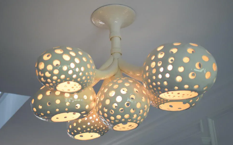 Ceiling-mounted sculptural lighting installation featuring perforated ceramic spheres and bowls with warm illumination casting intricate shadow patterns, designed by Newcomb Studios (Nicholas Newcomb Pottery & Sculpture).