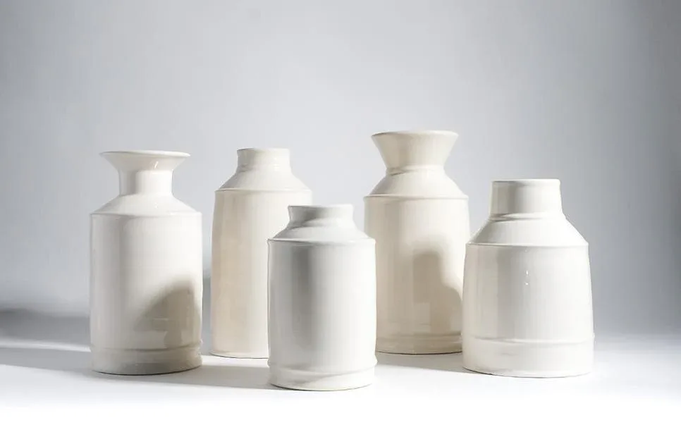 Five ceramic vessels with white glazed finishes and metallic silver accents arranged in a studio setting, showcasing pottery forms by Newcomb Studios.