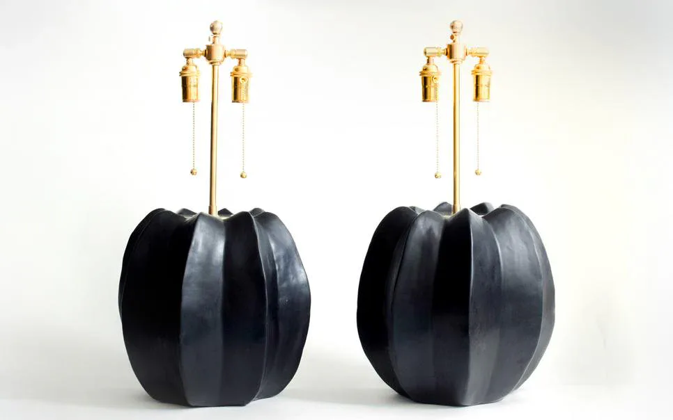 Pair of sculptural table lamps with bulbous black ceramic bases and brass multi-socket tops against a neutral background by Newcomb Studios.