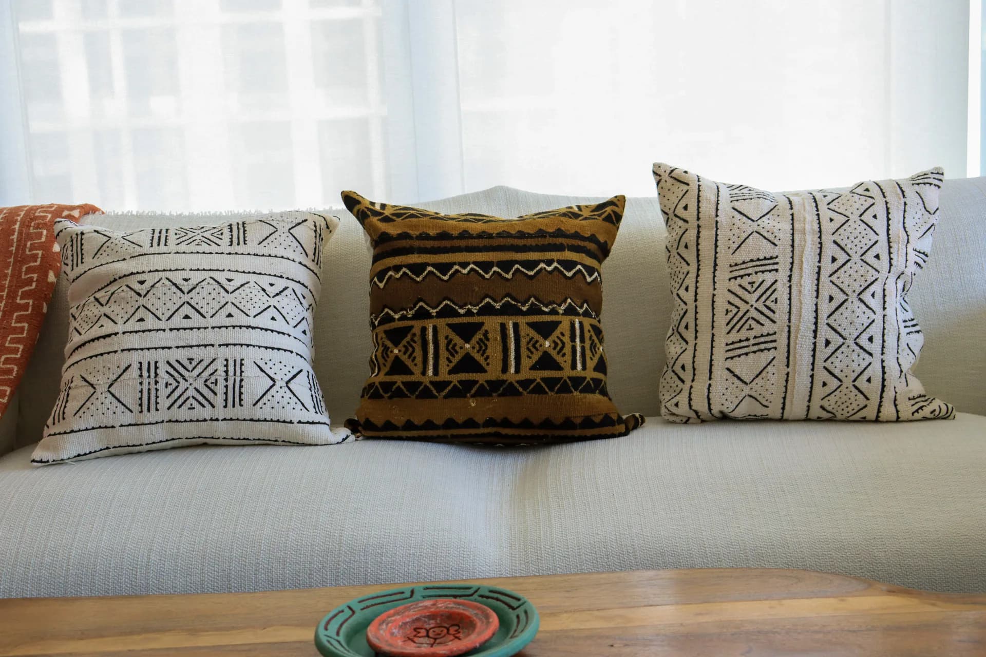 Light-filled living room featuring a cream upholstered sofa styled with three handwoven throw pillows in geometric patterns—rust, cream, and gold tones—by Niche Handmade Furniture.