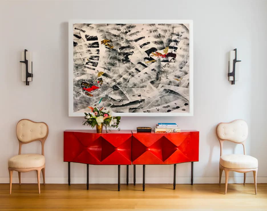 Modern living room with red geometric credenza, natural wood chairs, abstract artwork, and sculptural wall sconces by Nicole Fuller Interiors.