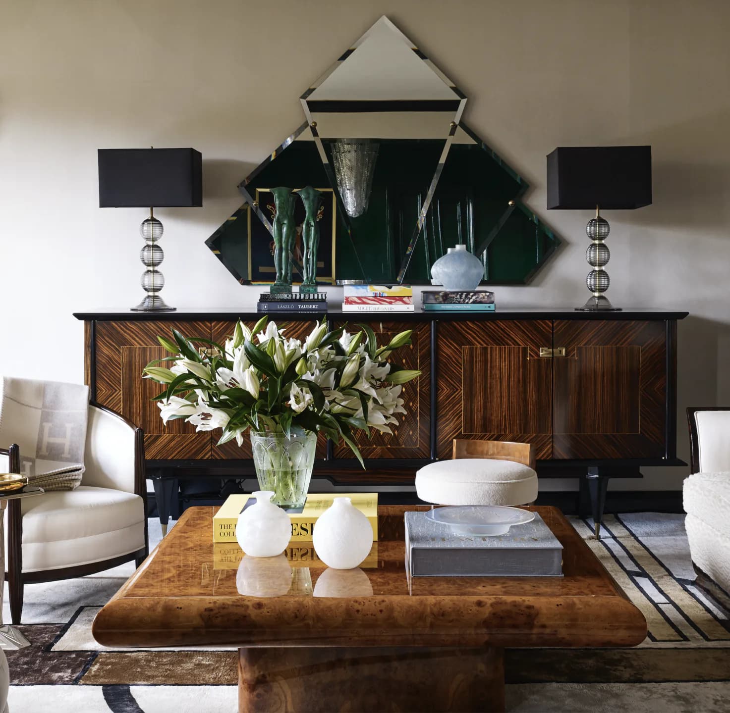 Luxurious living room featuring a dark wood credenza with white floral arrangement, geometric mirror above, layered lighting, and neutral seating by Nicole Fuller Interiors.