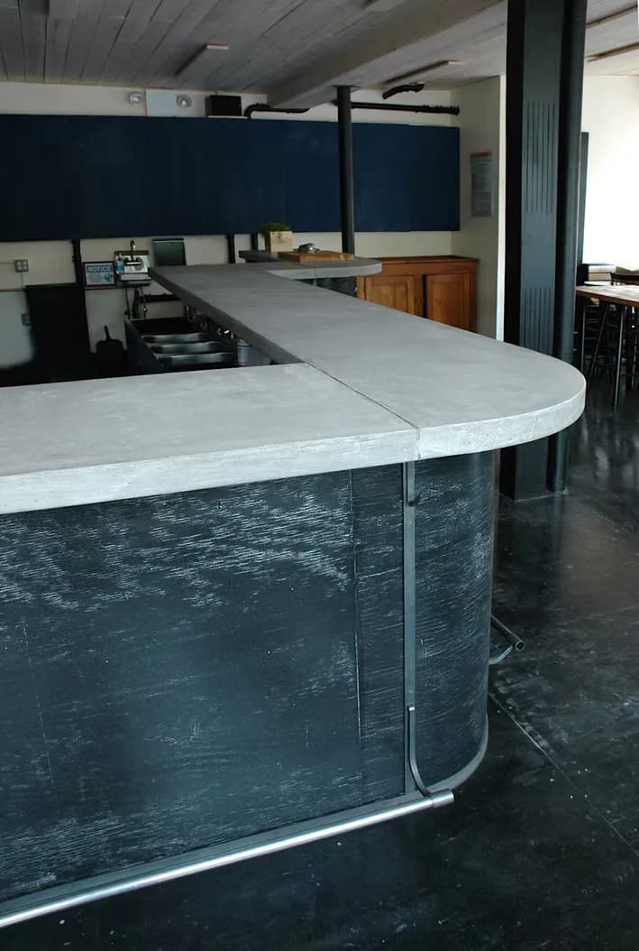 Curved reception desk with white countertop and dark textured base in minimalist interior with navy accent wall by Nine Stories.