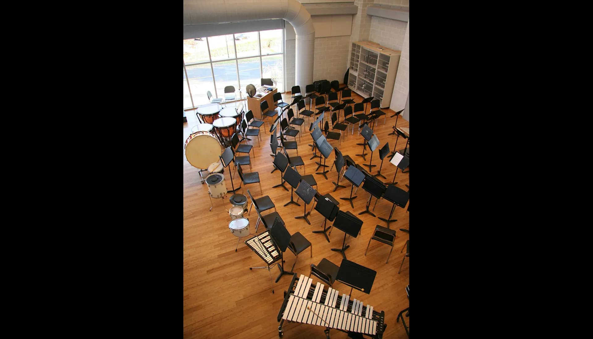 Music education studio with wooden flooring features multiple keyboard instruments and chairs arranged throughout a bright, windowed space by NK Architects.
