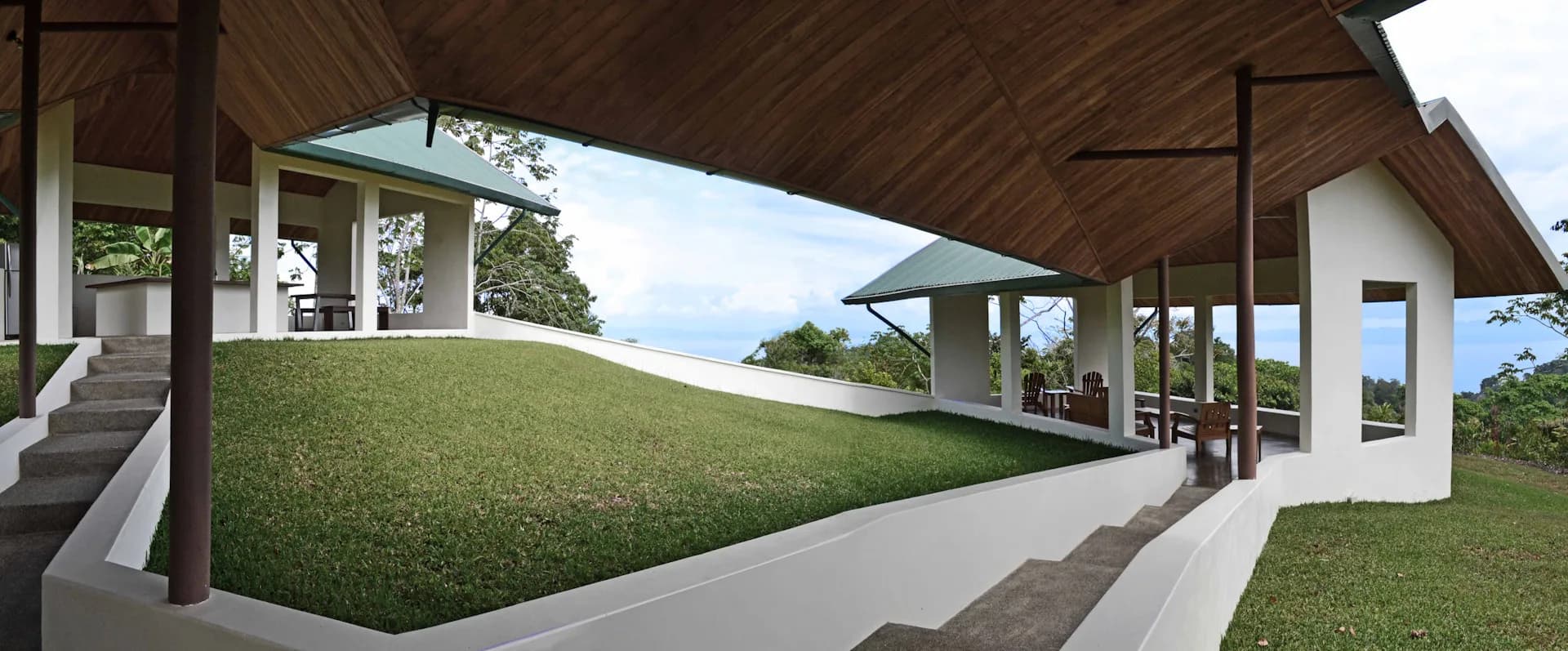 Modern architectural rendering of a covered pavilion with wooden ceiling, concrete walkway, and sloped green lawn by OBRA Architects.