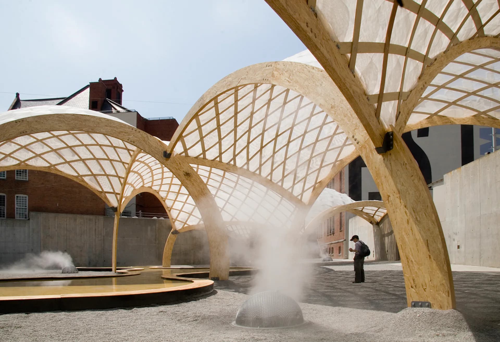 Wooden lattice pavilion with arched structures in courtyard space with mist installation, designed by OBRA Architects.