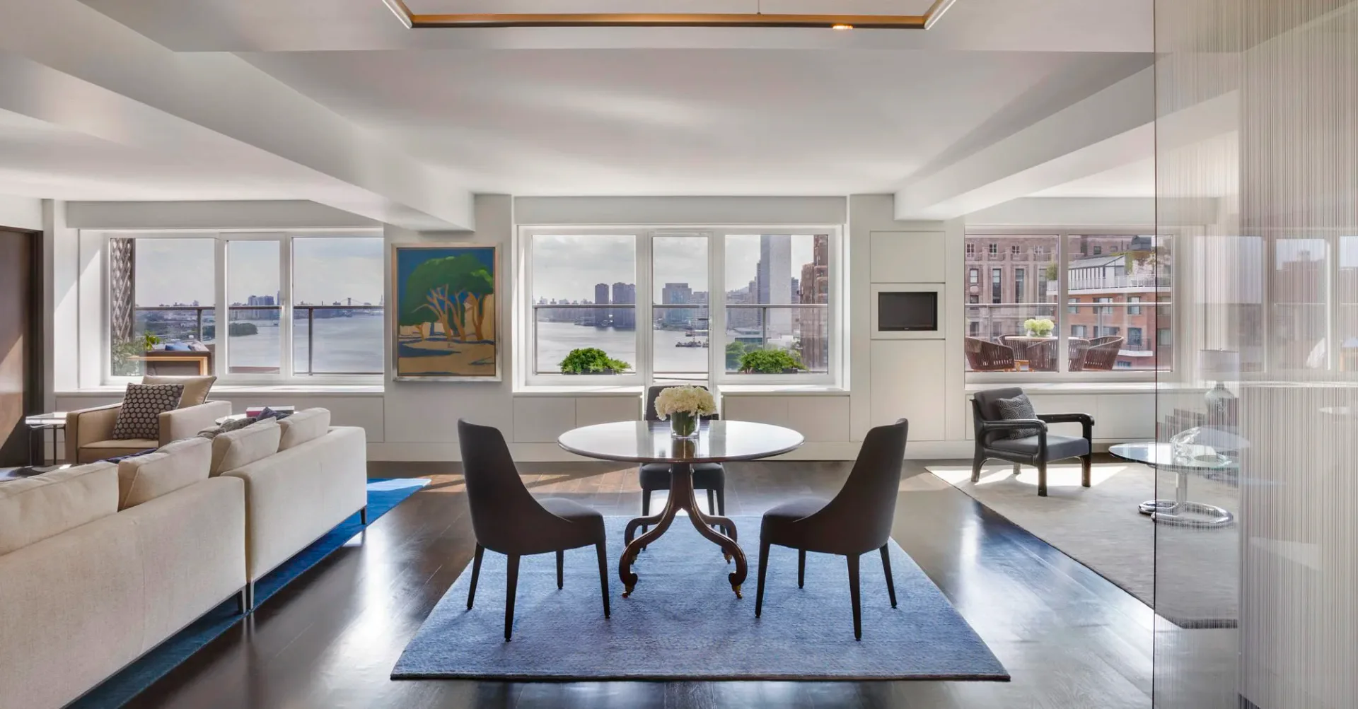 Modern luxury apartment with round dining table, black chairs, and blue area rug overlooking city skyline, designed by Odegard Carpets.