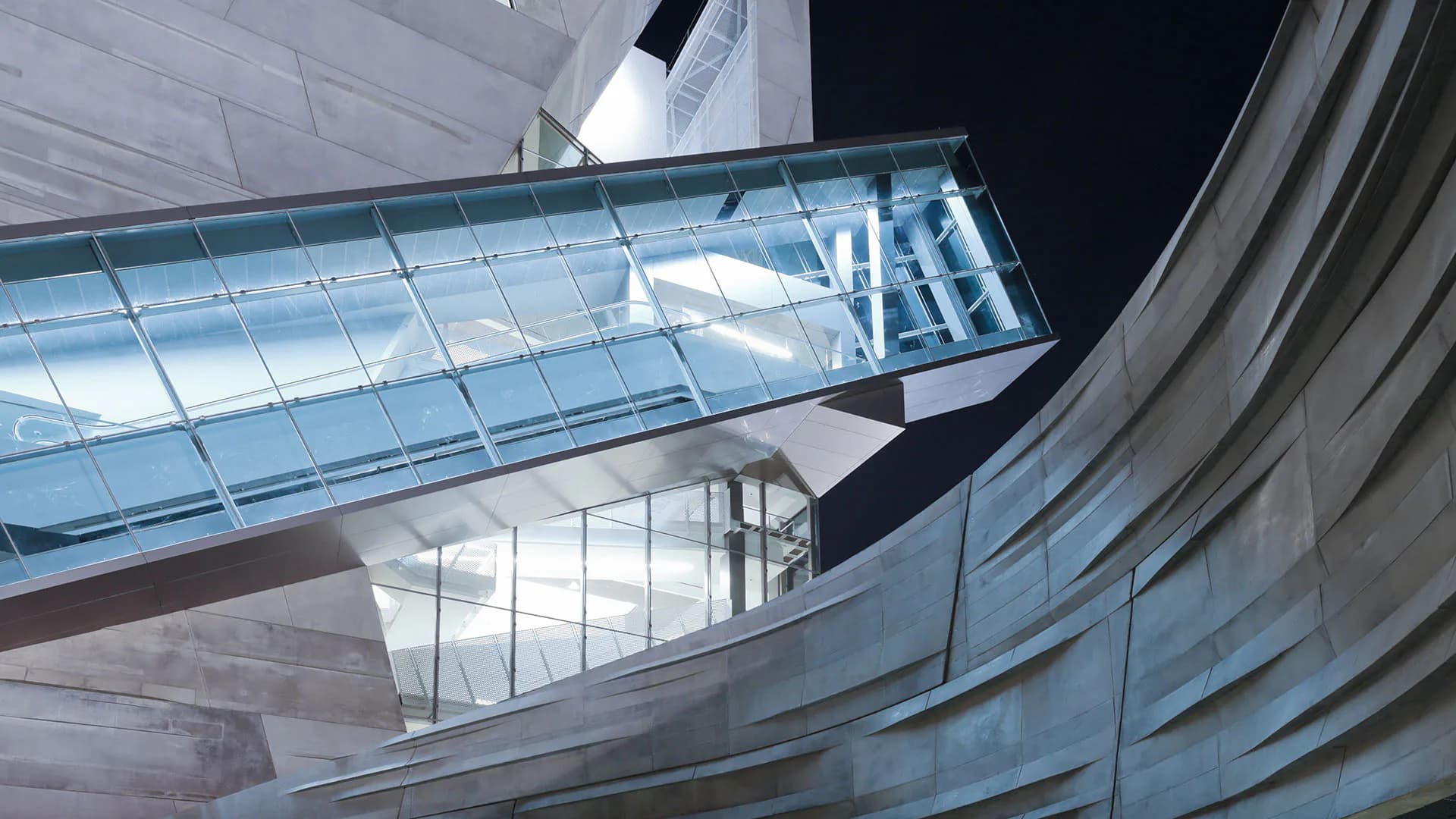 Modern architectural interior featuring curved white concrete walls, expansive glass skylights, and geometric metal framework creating dynamic interplay of light and shadow by Office for Visual Interaction (OVI).