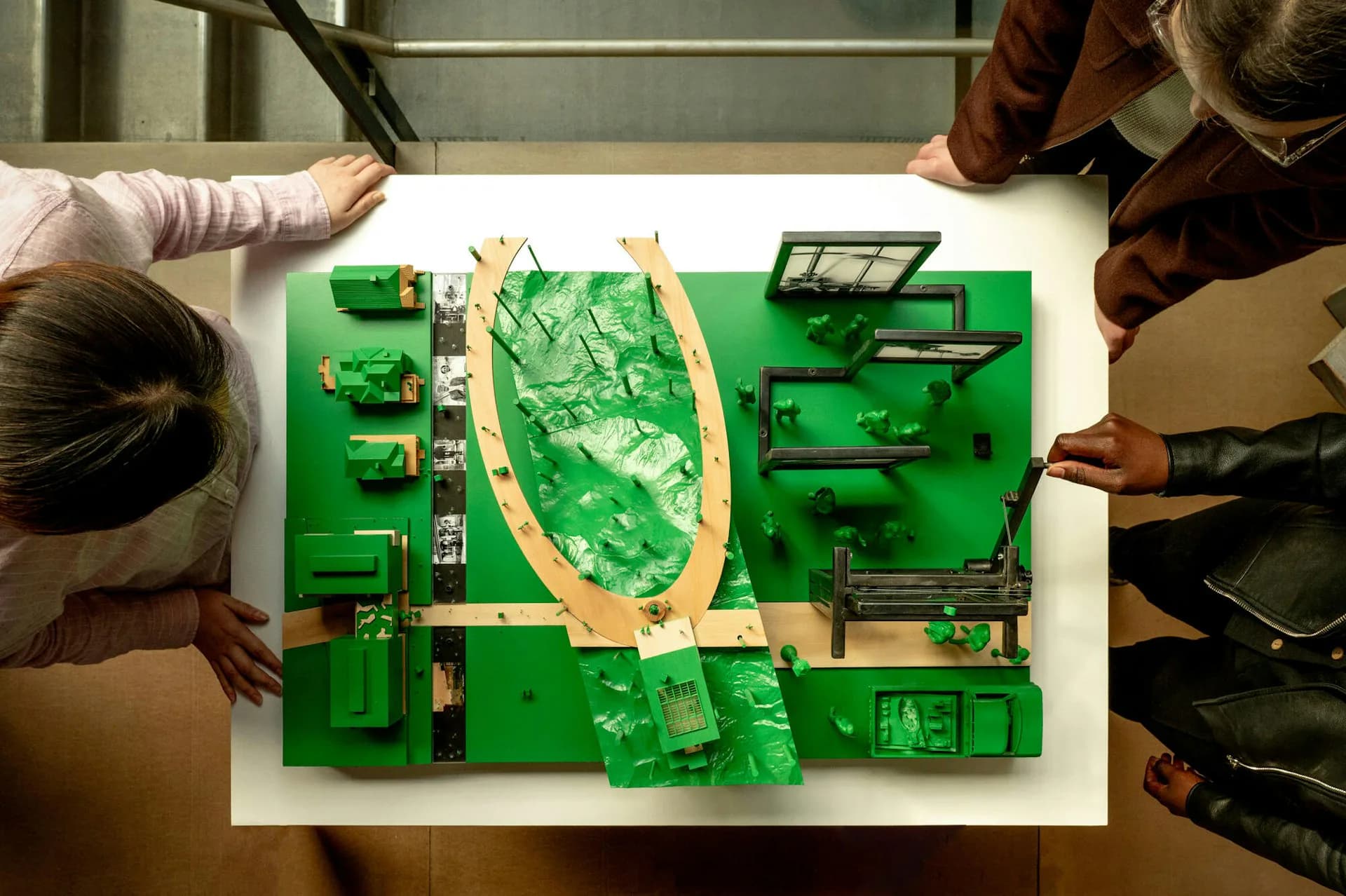 Overhead view of a green circuit board model with yellow marked pathways, examined by two people during a design workshop or presentation by Olson Kundig.
