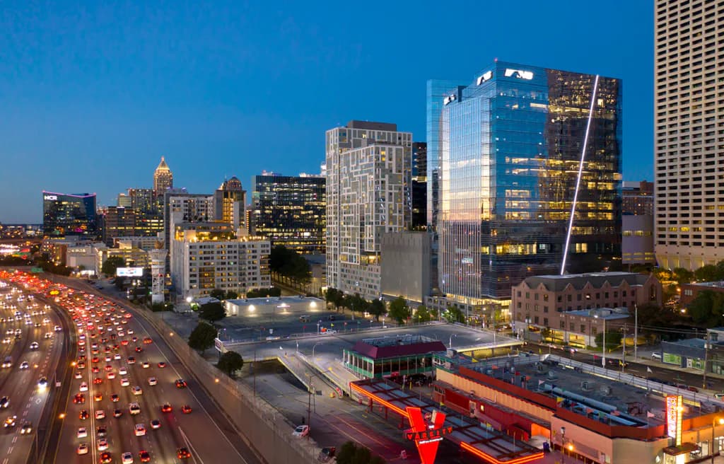 Downtown cityscape at dusk featuring illuminated high-rise buildings, busy highway with vehicle traffic, and red shipping containers in foreground by One Lux Studio.