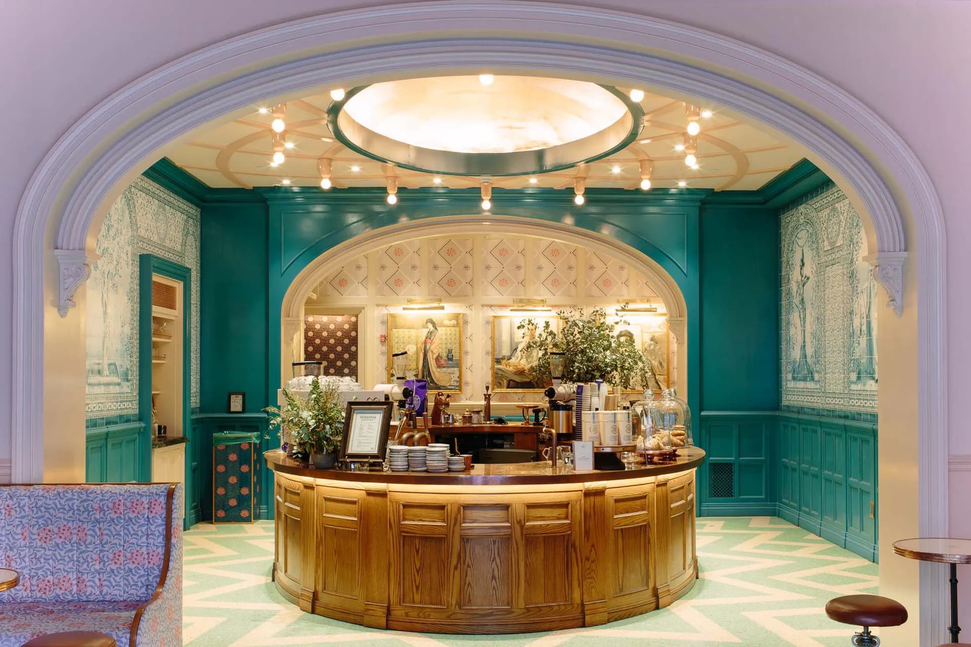 Luxurious hotel lobby with teal-green paneled walls, curved wooden reception desk, arched ceiling with integrated lighting, and elegant cream and gold finishes by One Lux Studio.