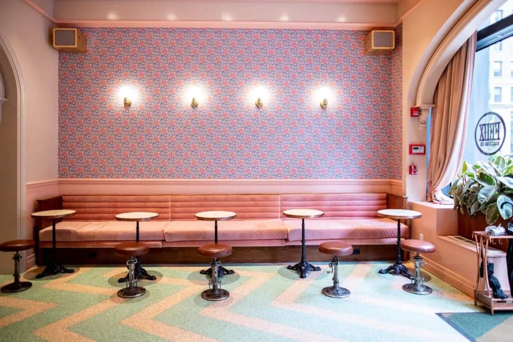 Modern waiting area with extended pink banquette seating, geometric patterned carpet, brick accent wall with recessed lighting, and arched window by One Lux Studio.