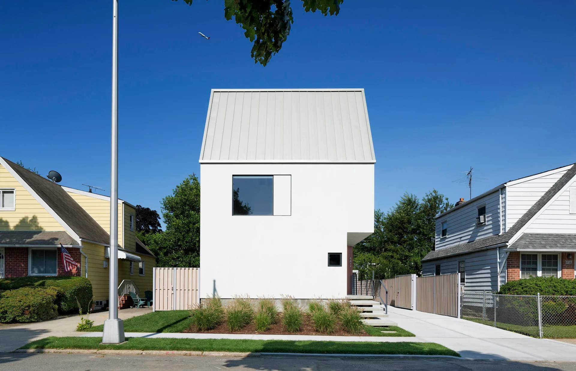 Modern white cubic residential building with metal roof and minimal fenestration sits among traditional suburban homes, designed by O'Neill Rose Architects.